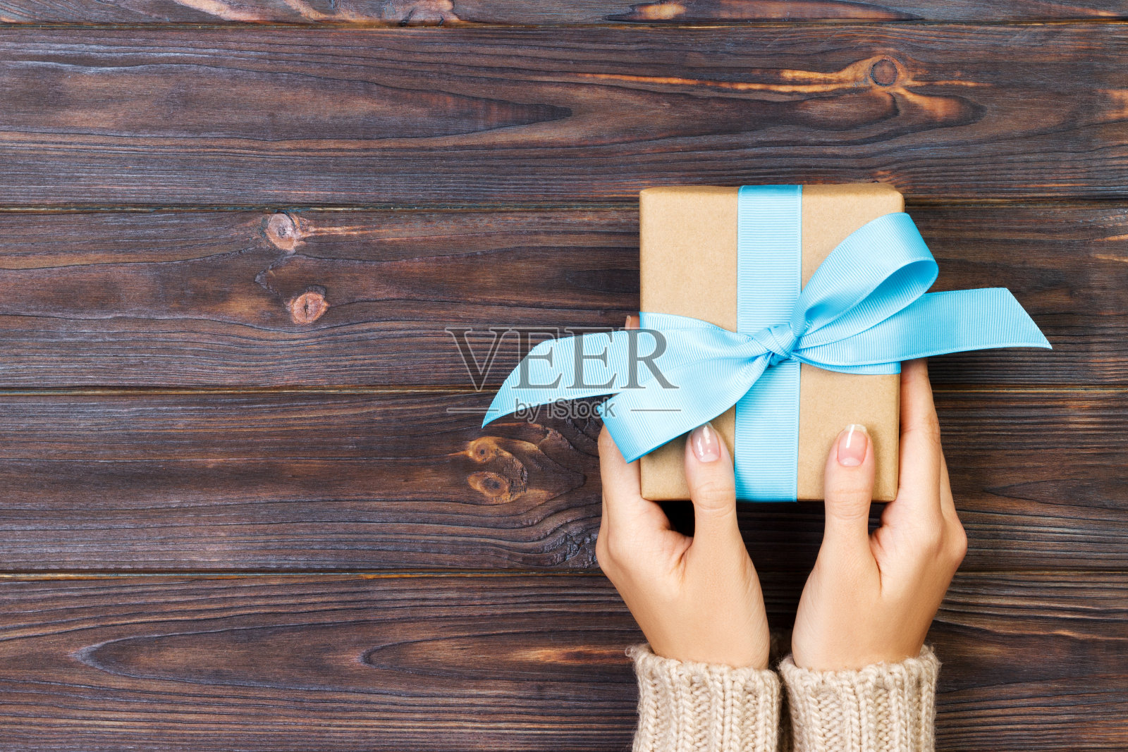 女人的手给包裹情人节或其他节日手工礼物在纸与蓝色丝带。礼品盒，礼品装饰在白色木桌上，顶视图与拷贝空间照片摄影图片