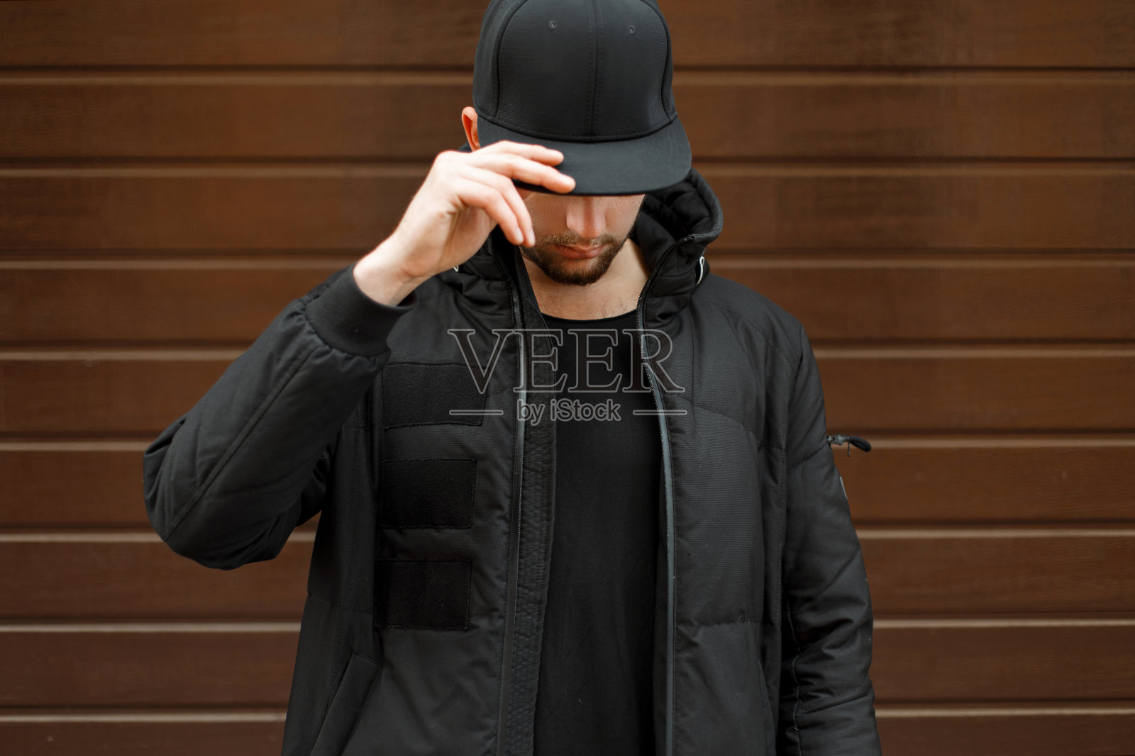 一名年轻人戴着一顶时尚的黑色棒球帽，穿着一件冬装夹克在街上摆姿势照片摄影图片