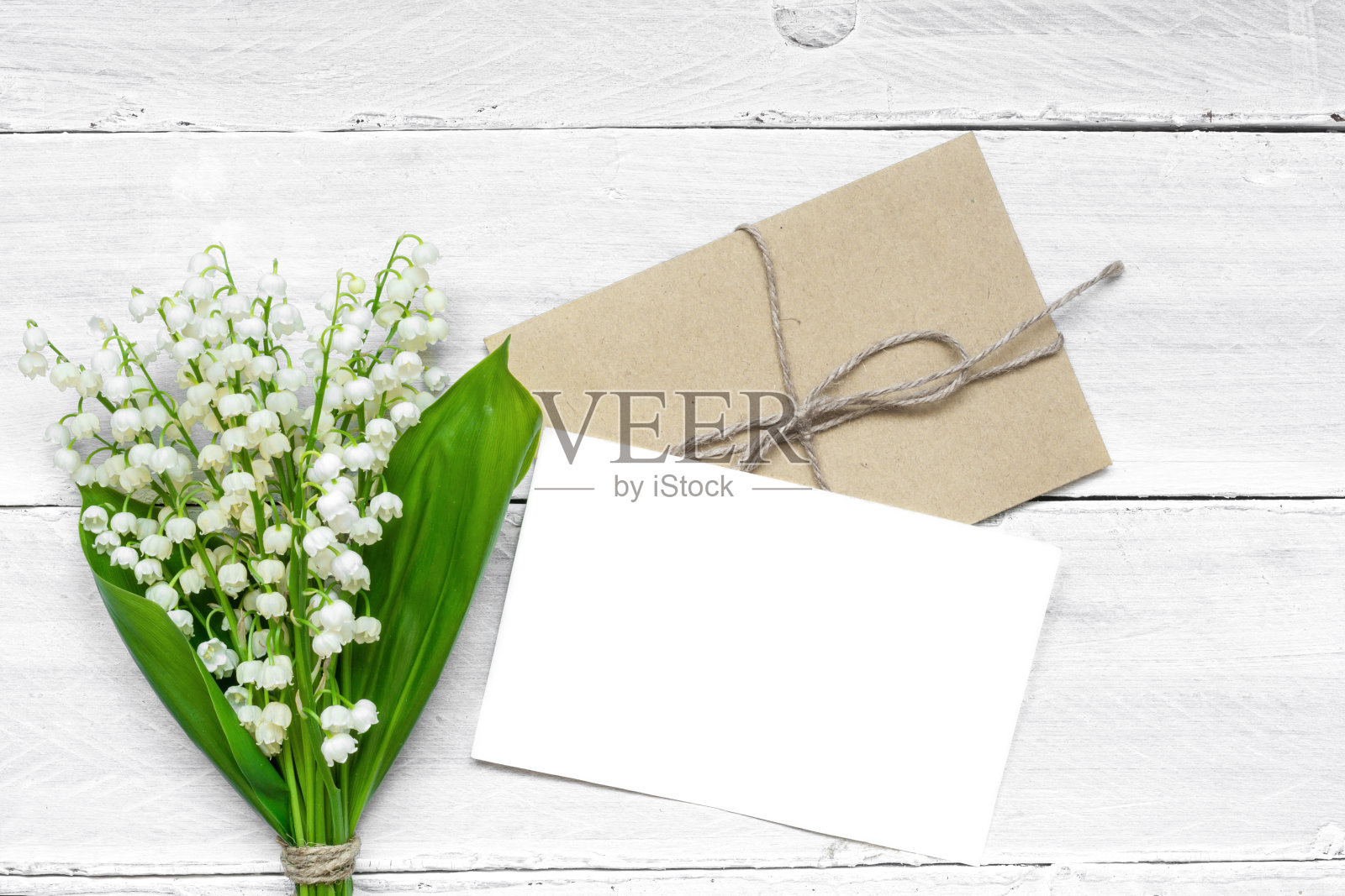 空白的白色贺卡和信封与春天的山谷百合的花朵和蓓蕾照片摄影图片