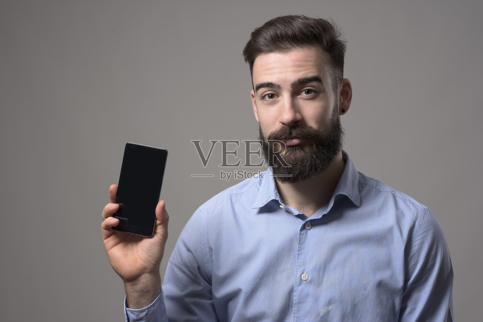 年轻的大胡子商人或程序员在智能手机空白屏幕上做广告照片摄影图片