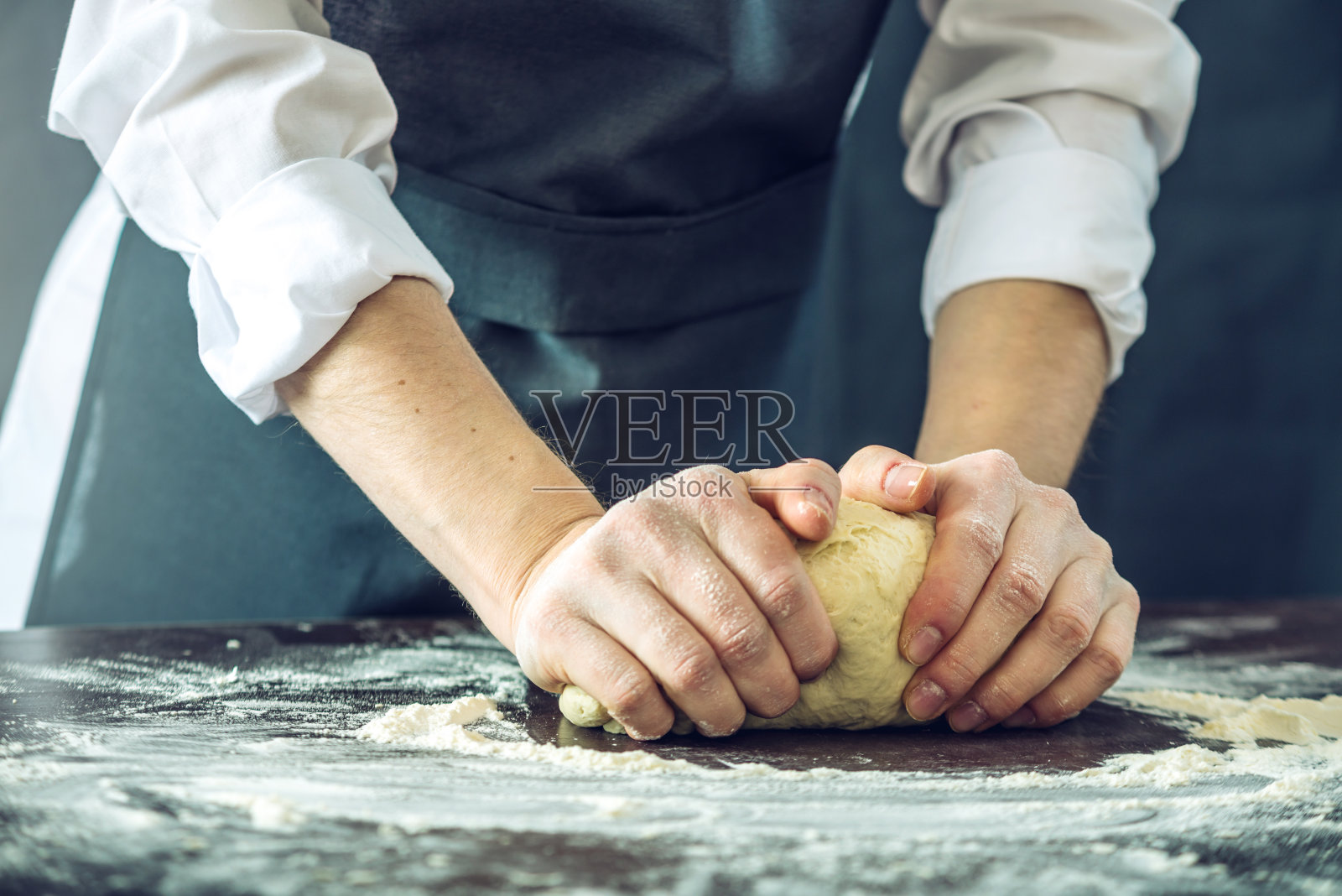 穿着黑围裙的厨师用你的手在桌子上做披萨面团照片摄影图片