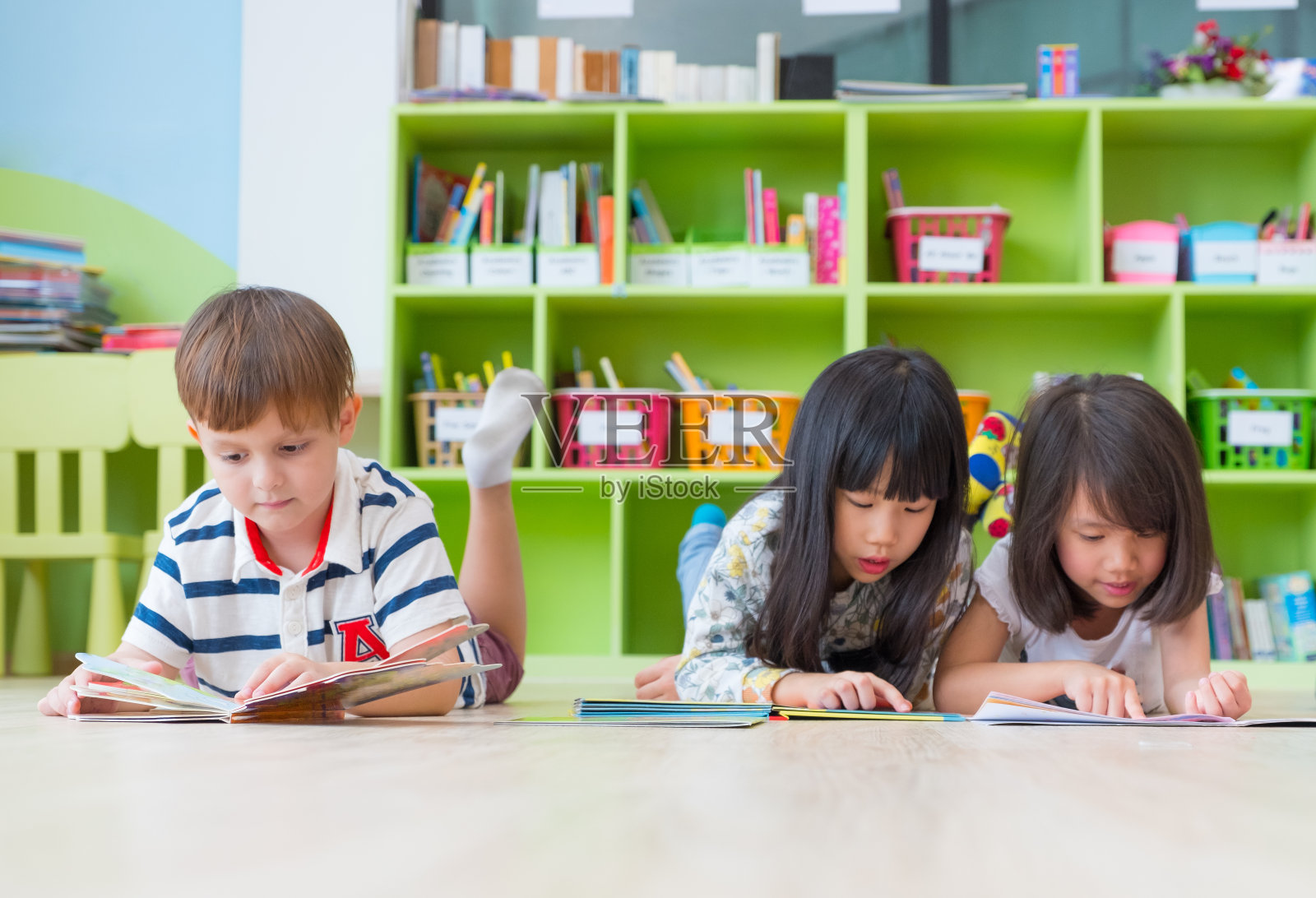 多元化幼儿躺在幼儿园图书馆的地板上阅读童话书，幼儿园的教育理念照片摄影图片