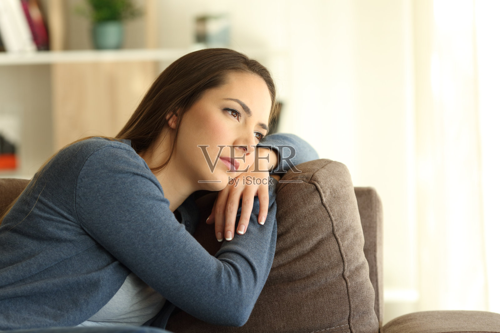 一个悲伤的女人坐在沙发上透过窗户看照片摄影图片