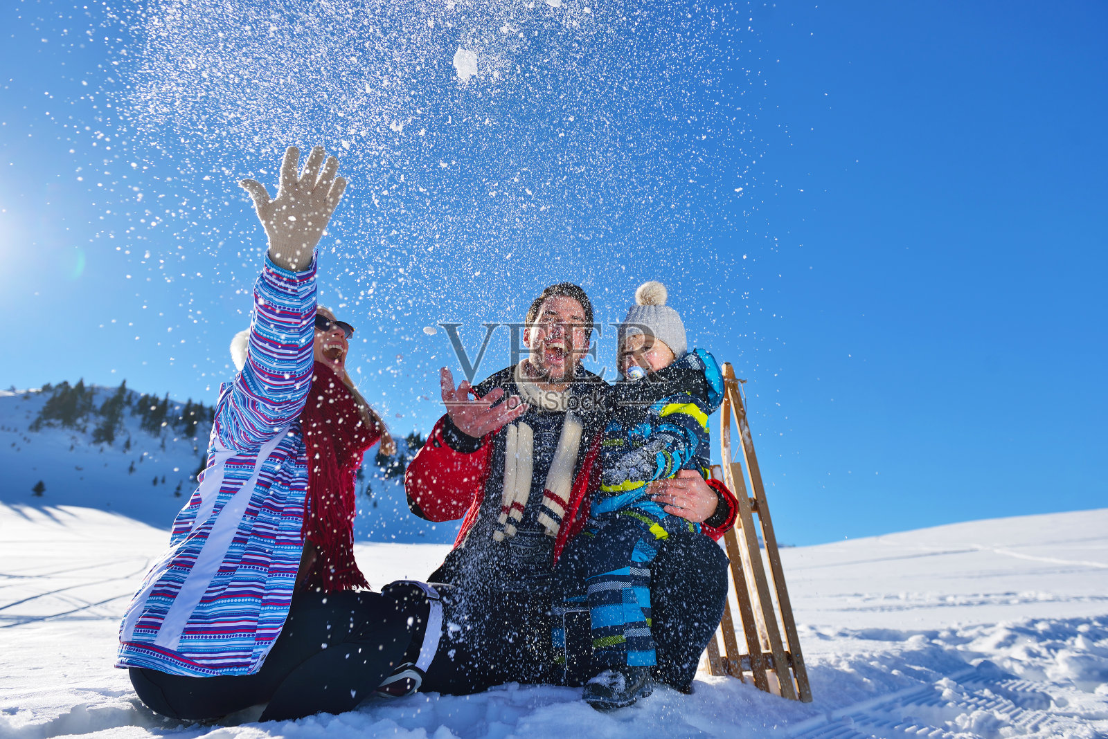 在美丽阳光明媚的冬日户外，快乐的年轻家庭在新鲜的雪中玩耍照片摄影图片