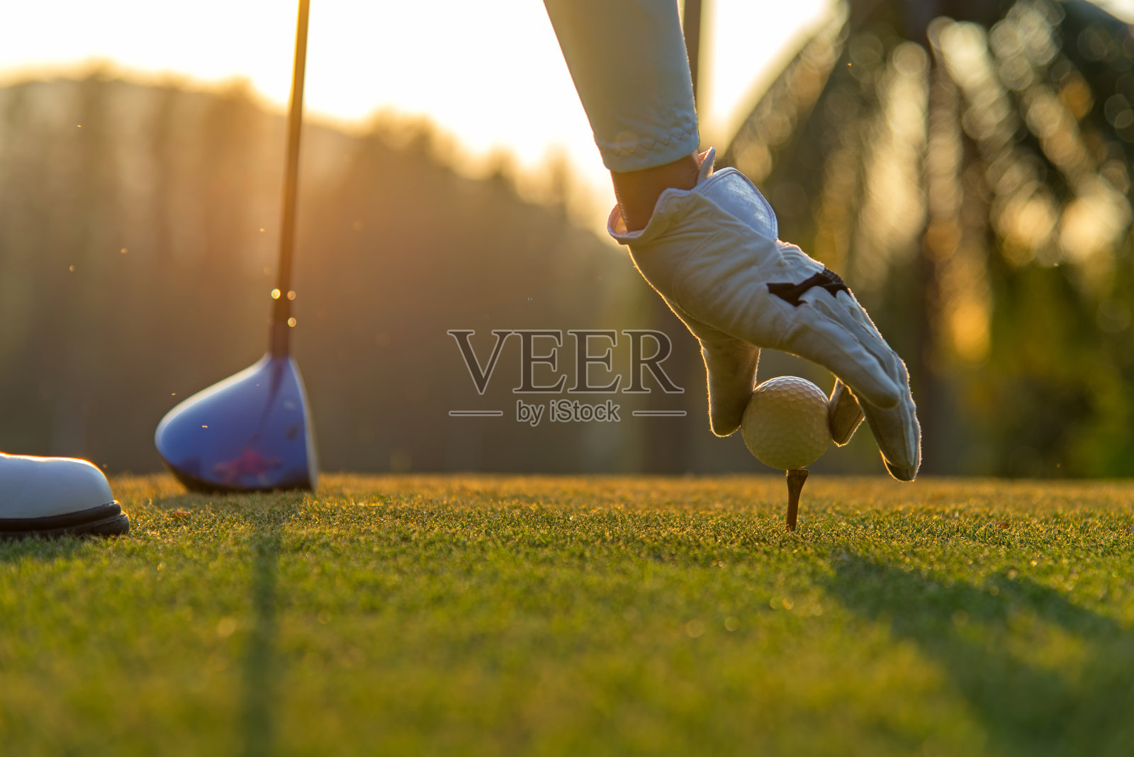 在傍晚和日落时分，亚洲妇女在高尔夫球场用球杆把高尔夫球放在球座上，这是一项有益于健康的运动。生活方式的概念照片摄影图片