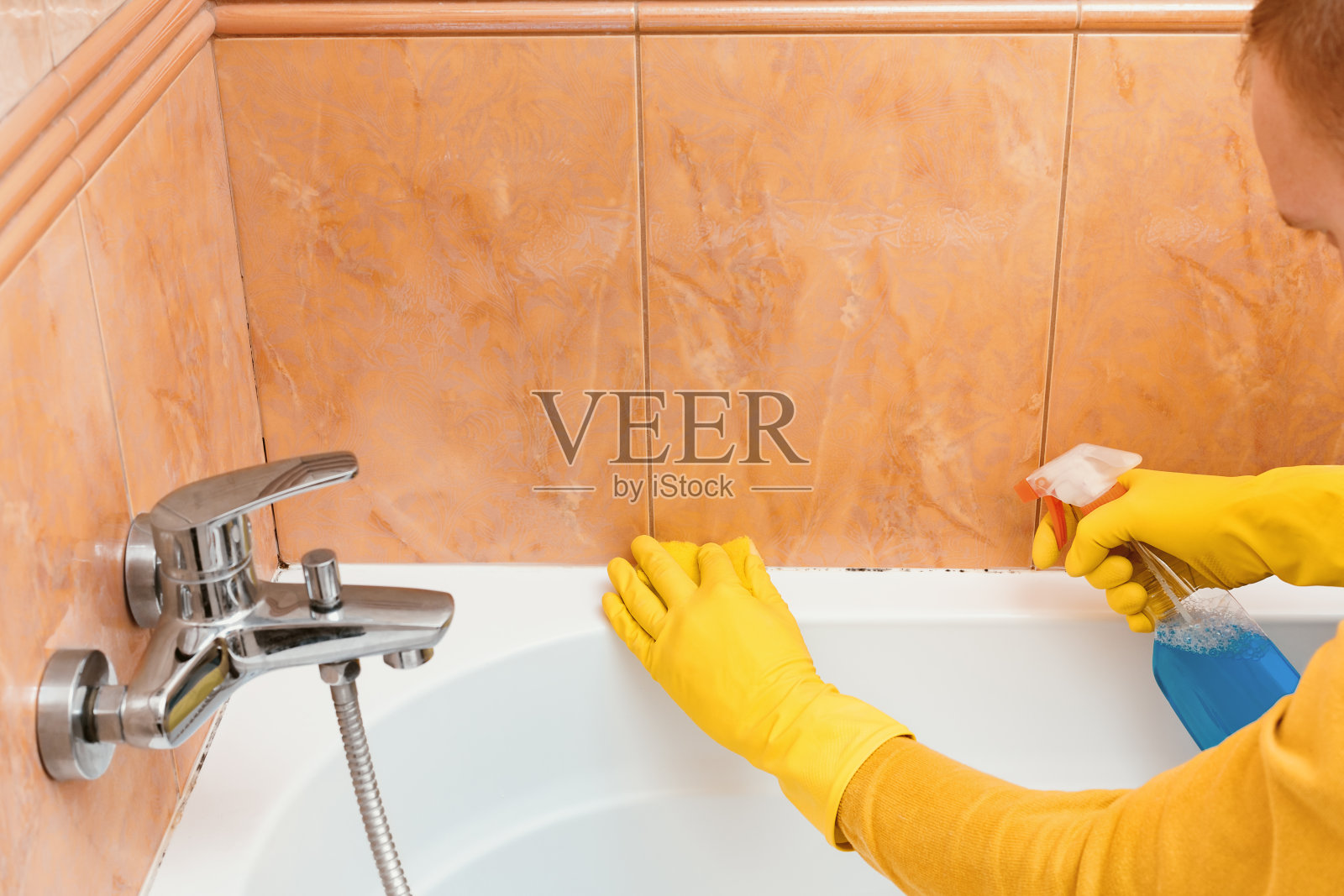 男子用海绵和清洁用品清洗浴室，以去除霉菌照片摄影图片