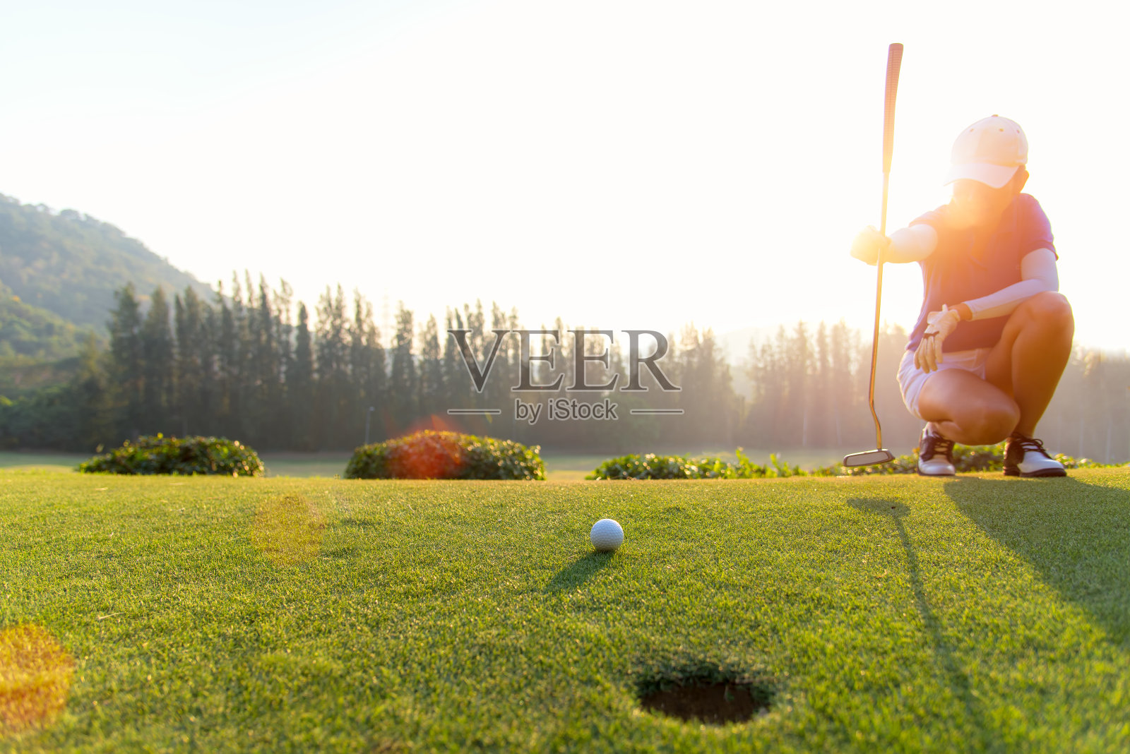 亚洲女子高尔夫球运动员在推球前蹲和研究果岭。生活方式的概念照片摄影图片