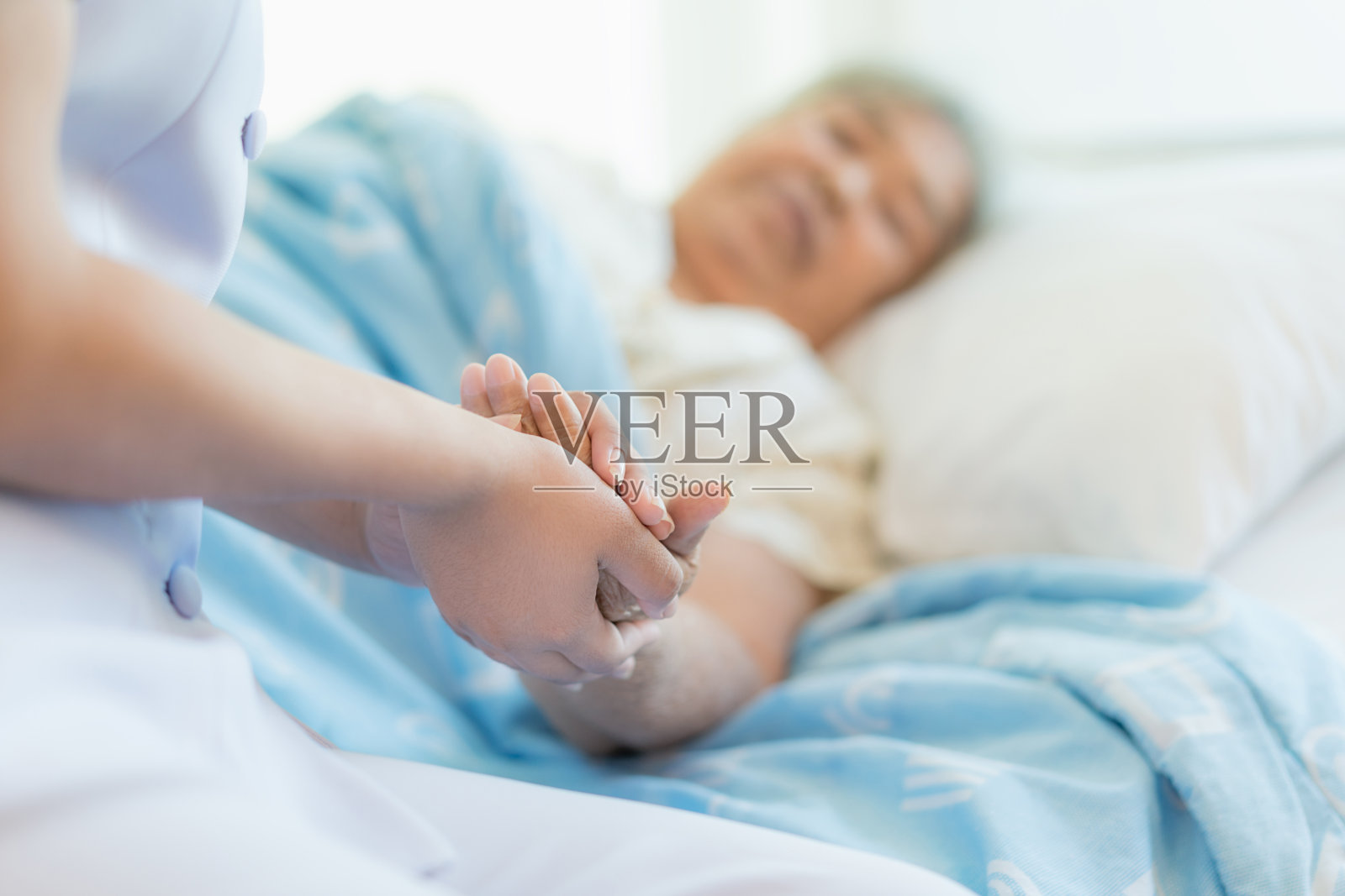 护士坐在医院病床旁，旁边一名老年妇女伸出援手，照顾老人的概念照片摄影图片