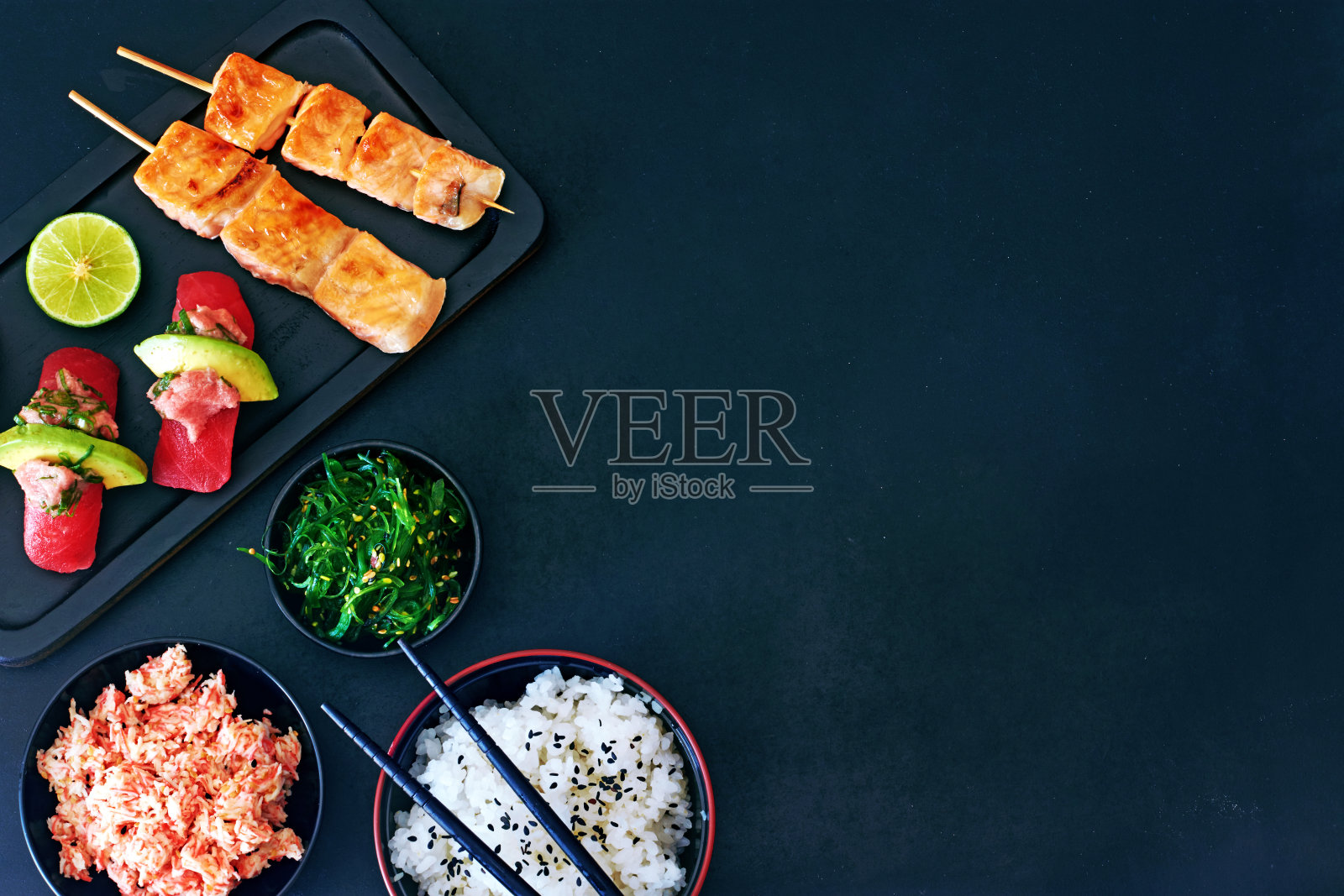 俯视图金枪鱼寿司，烤三文鱼串，碗或米饭，蟹肉和裙带菜沙拉在深色的板上复印空间。照片摄影图片