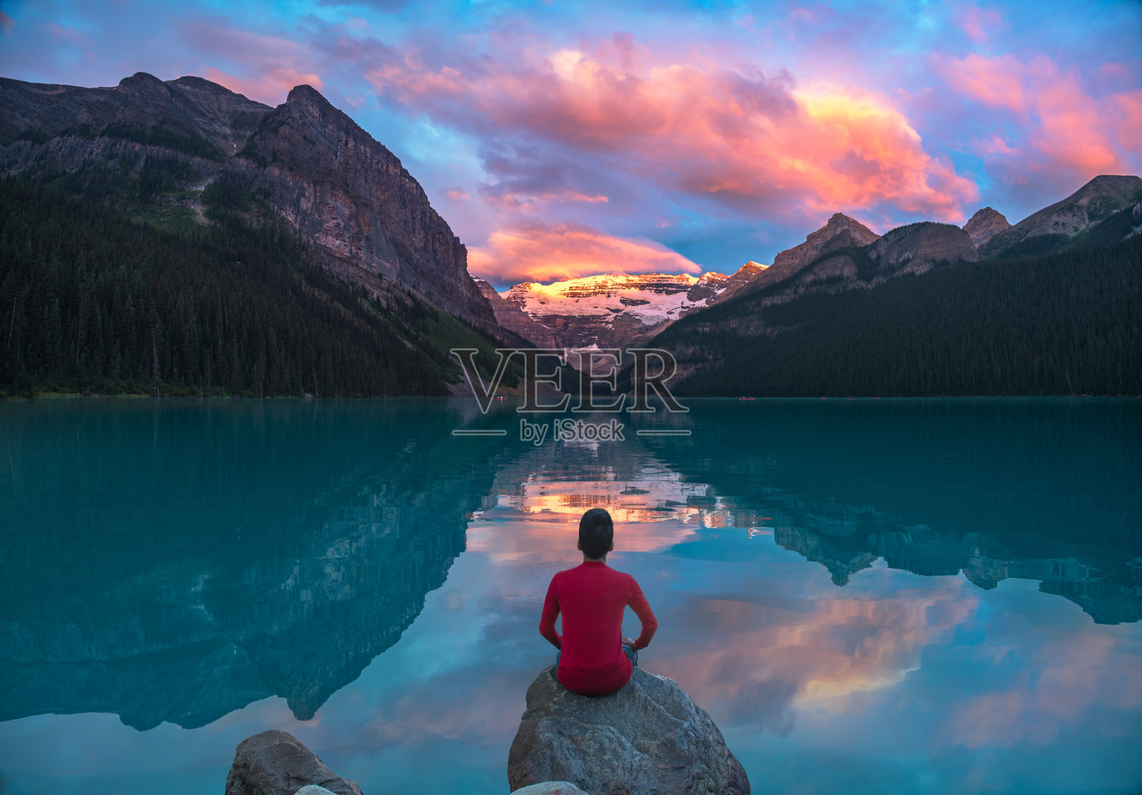 一名男子坐在岩石上观看露易丝湖晨云的倒影照片摄影图片