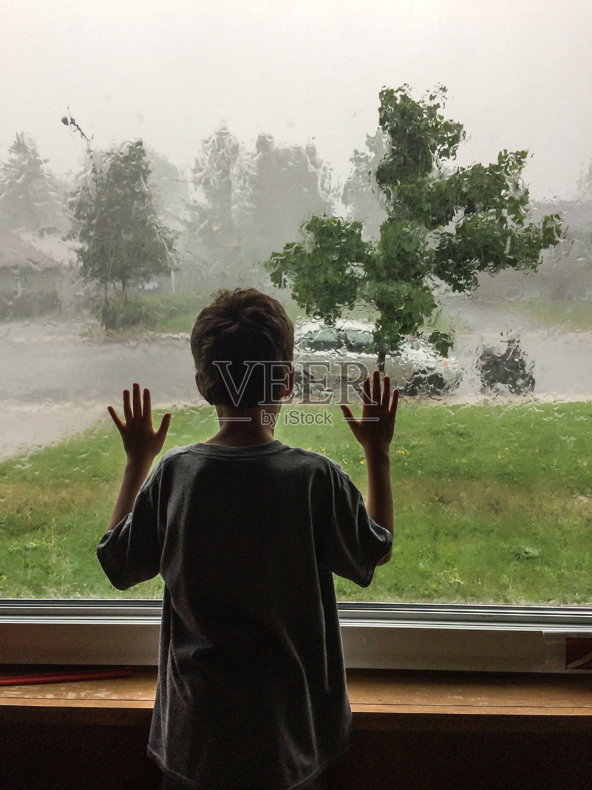 小男孩从后面透过客厅的窗户看着暴风雨照片摄影图片