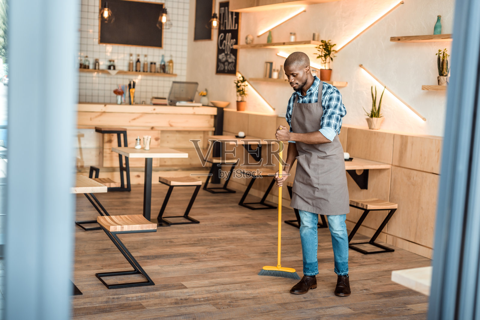 英俊的非裔美国工人在咖啡店用扫帚扫地照片摄影图片