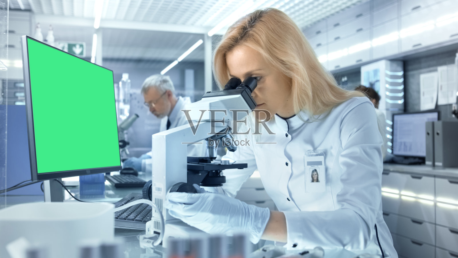 女性研究科学家在显微镜下观察生物样本。她和她的同事们在一家大型现代化实验室/医疗中心工作。照片摄影图片