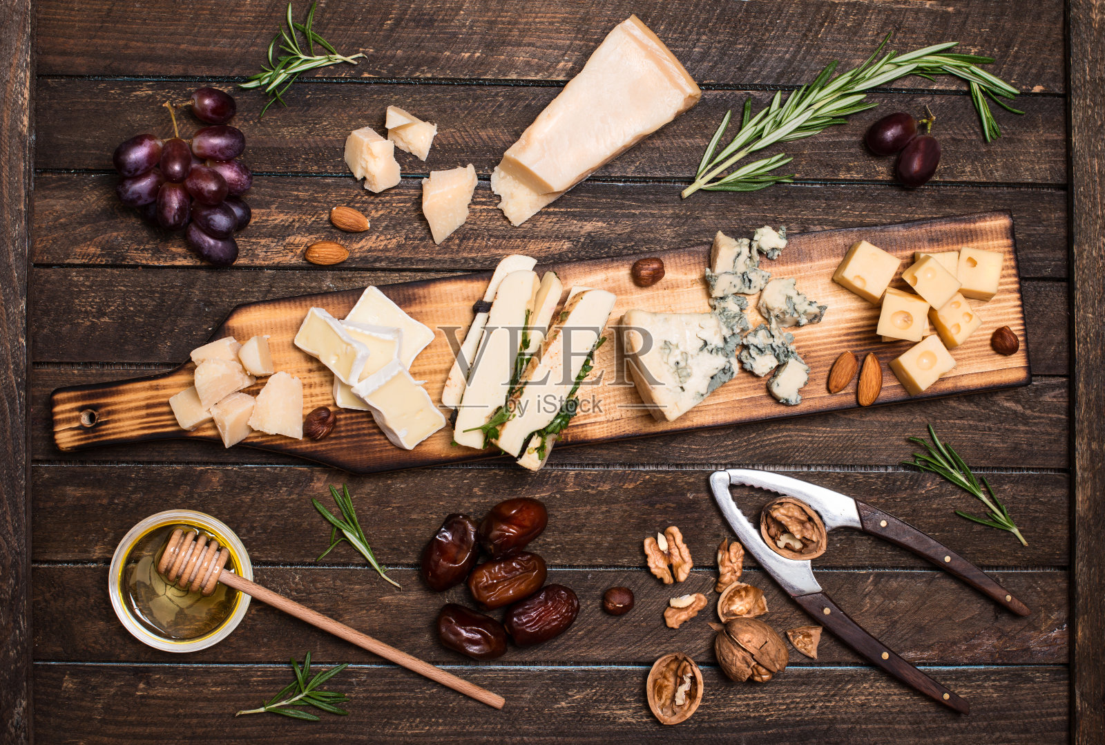奶酪拼盘与不同的奶酪，葡萄，坚果，蜂蜜，面包和枣在乡村木制背景。在深色木板上选择复古风格的奶酪品种。照片摄影图片