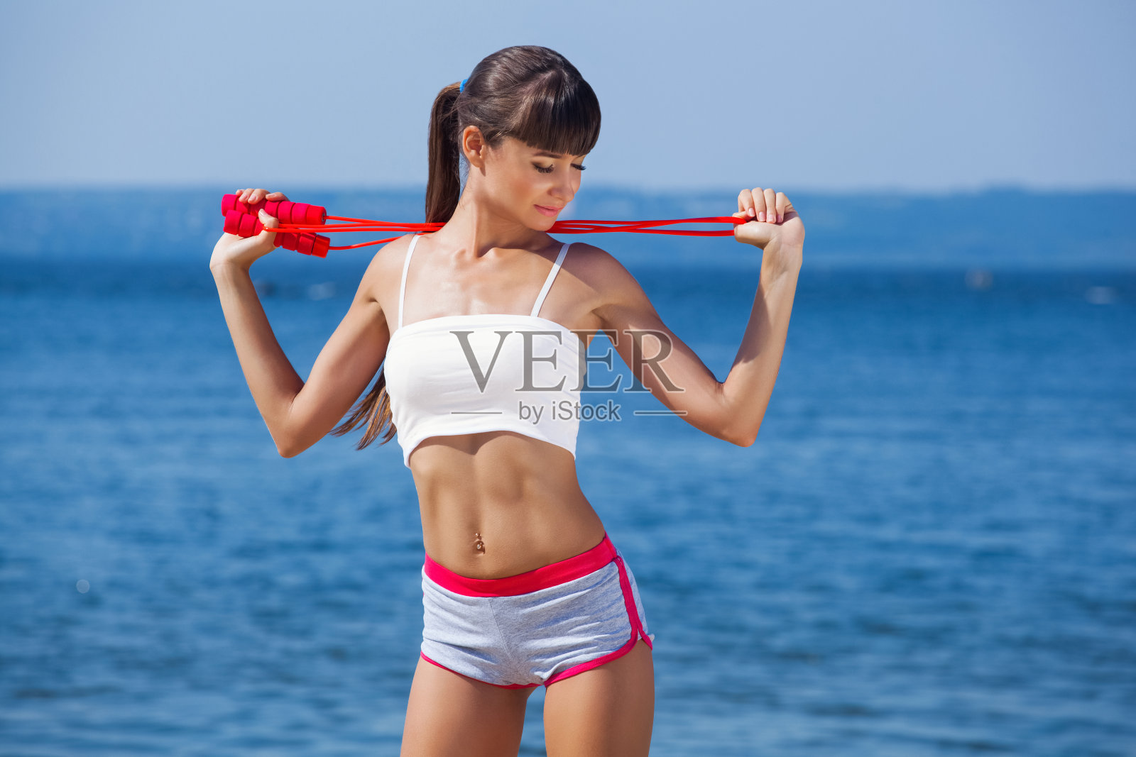 美丽的体育女子手中拿着一根红色的绳子，在大海的背景下从事着体操照片摄影图片