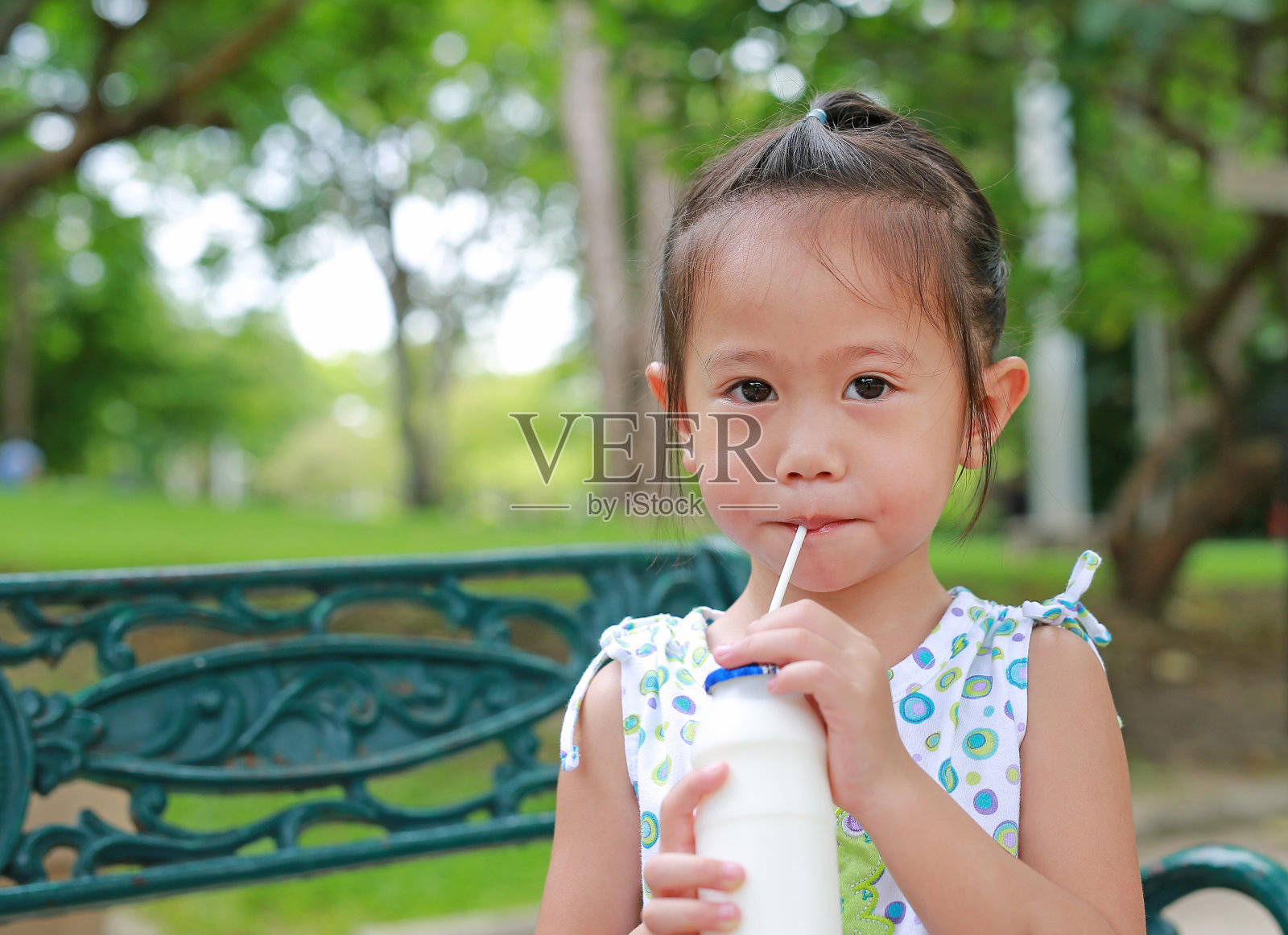 小女孩在公园里用稻草喝牛奶。照片摄影图片