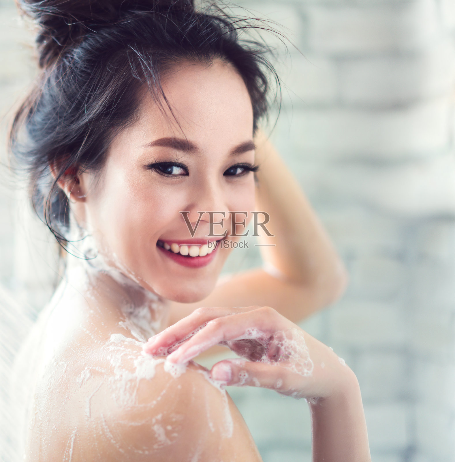 亚洲妇女正在浴室洗澡，她擦肥皂，她是快乐和放松。照片摄影图片