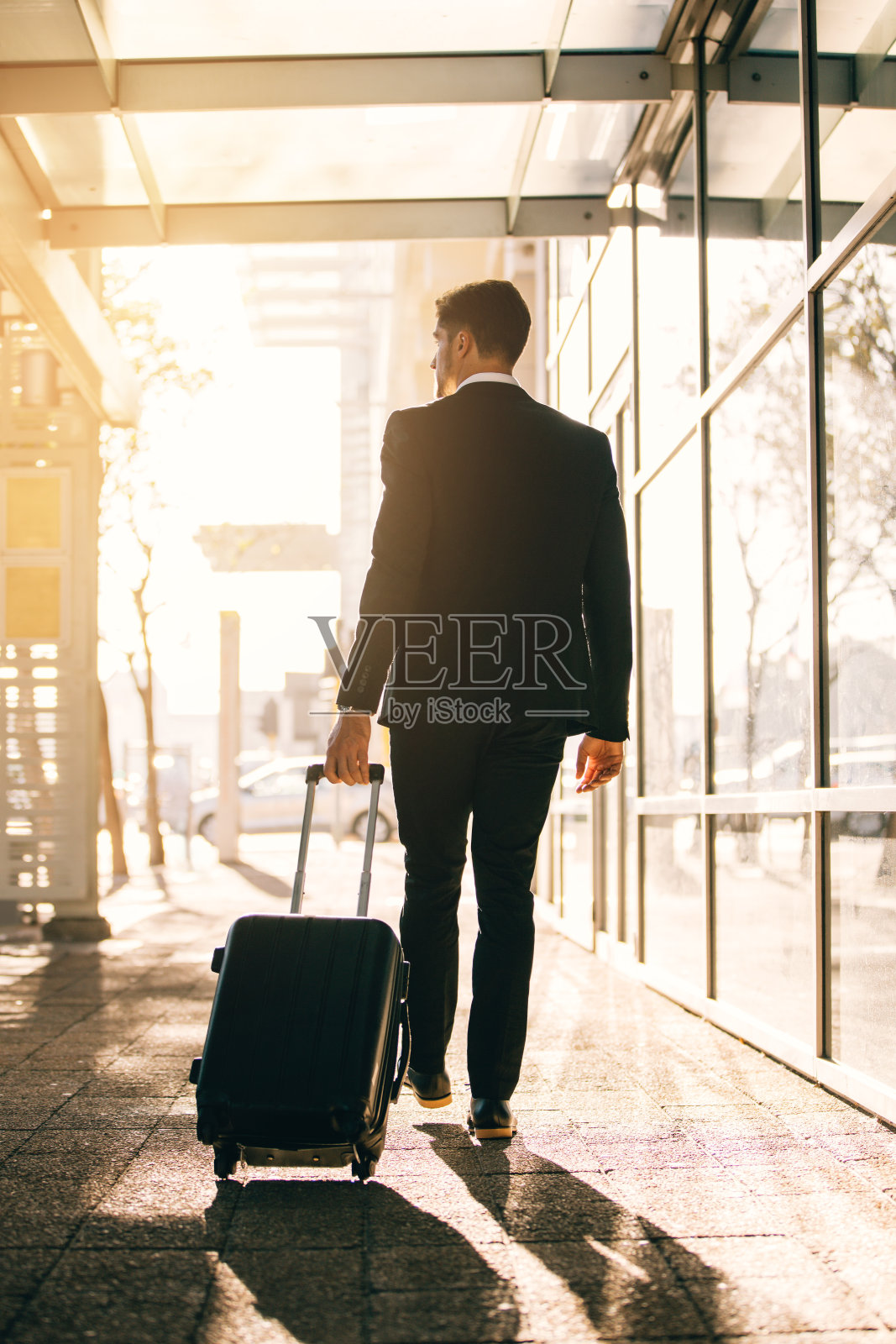 年轻的商人提着行李箱走在机场大楼外照片摄影图片