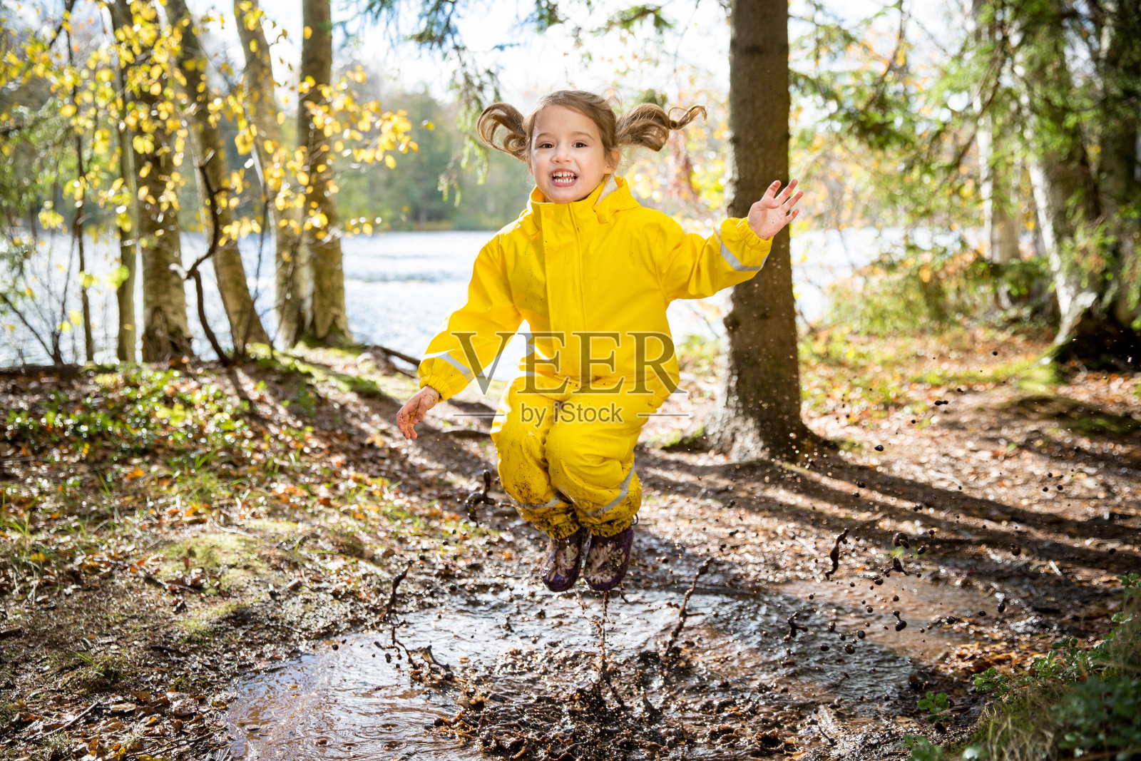 可爱的小女孩在泥泞的水坑里跳照片摄影图片