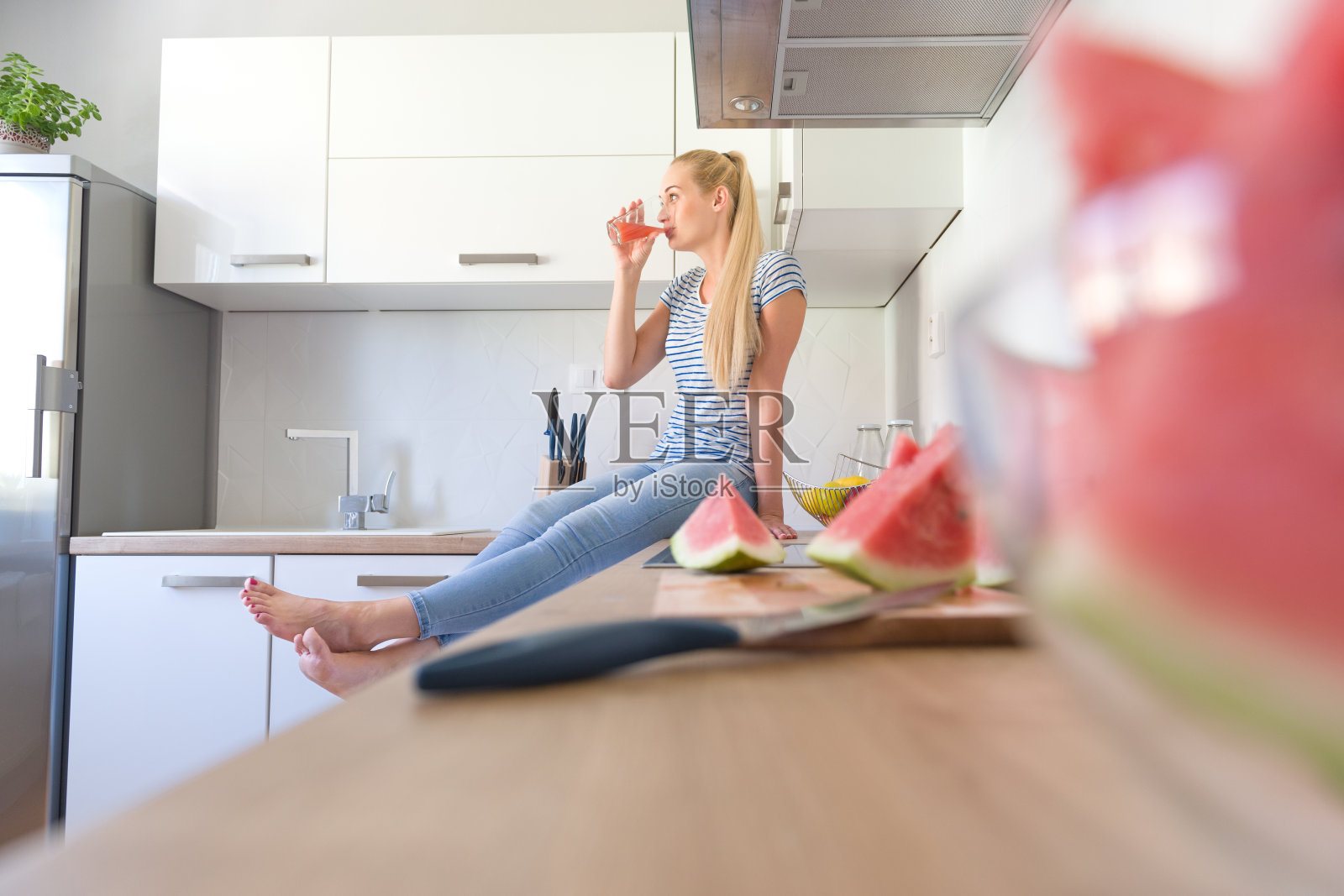 坐在厨房柜台上喝果汁的女人。照片摄影图片