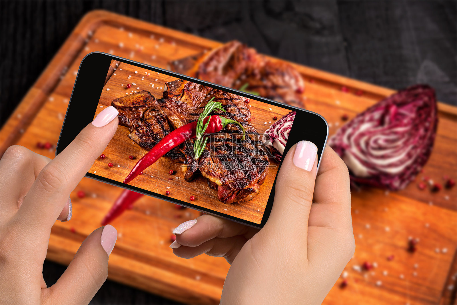 拍摄食物概念——游客用智能手机在切好的木板上拍摄即食牛排照片摄影图片