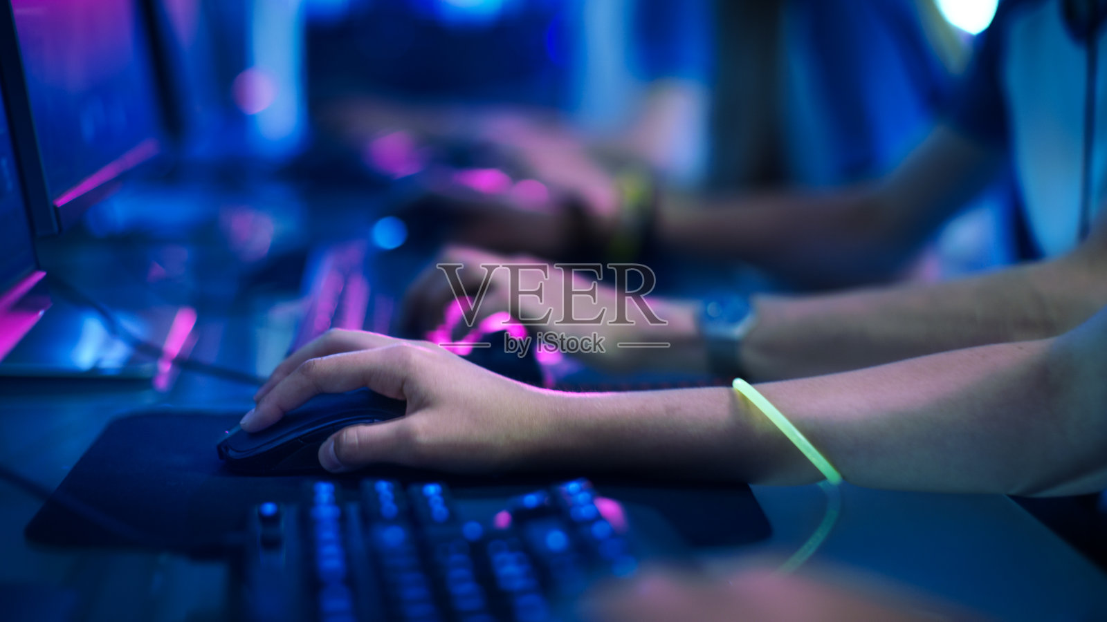 特写在一排玩家的手在键盘上。jpg，积极推动按钮，玩MMO游戏在线。背景是霓虹灯。照片摄影图片
