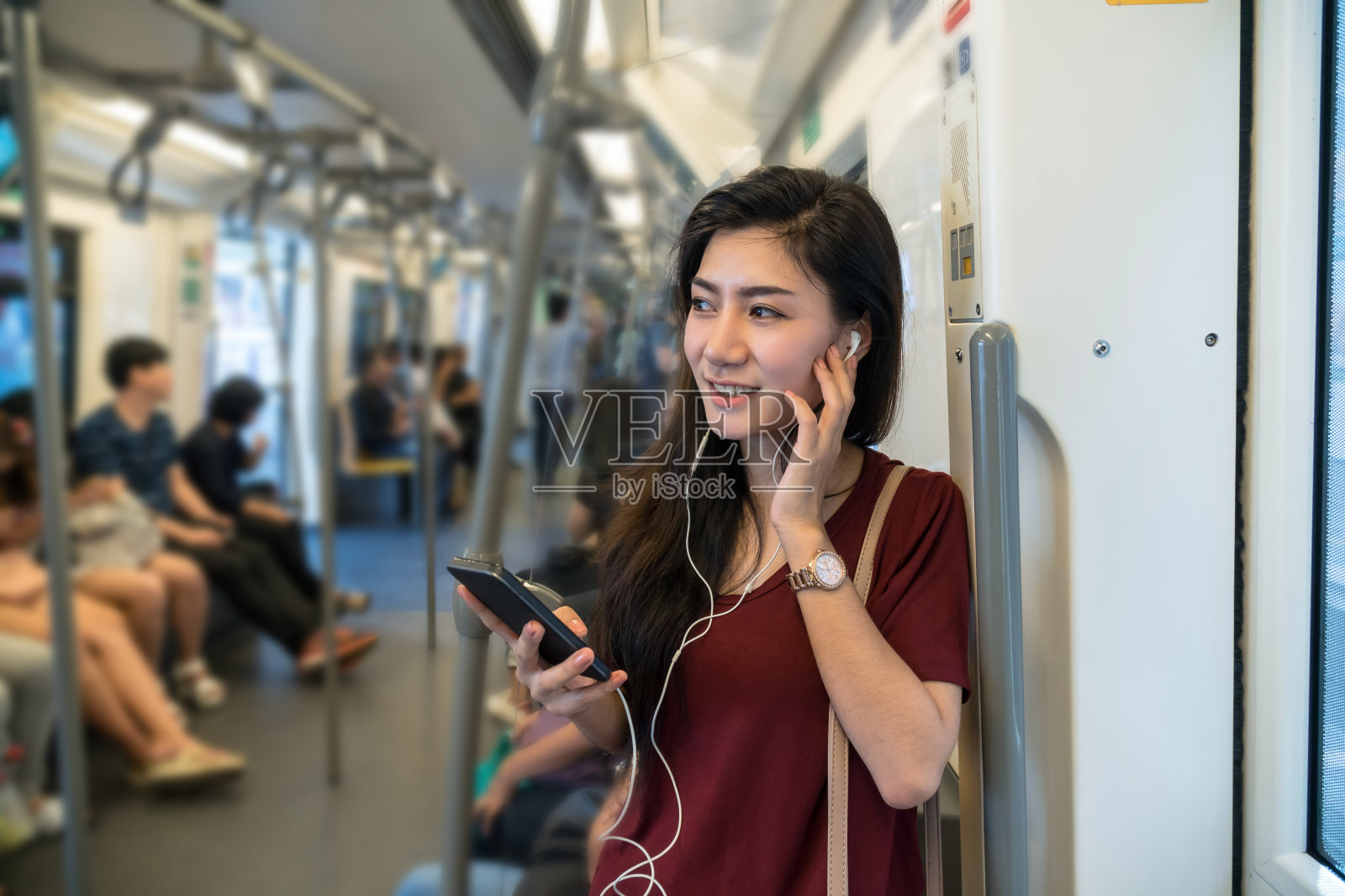 亚洲女性乘客穿着休闲服装，通过智能手机在BTS轻轨或捷运地铁上使用和听这首歌，在大城市旅行，生活方式和交通理念照片摄影图片