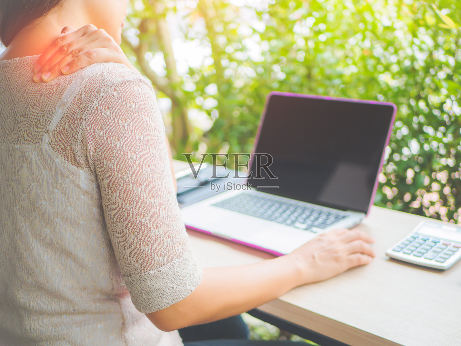 一名妇女在长时间使用电脑后感到疼痛时，把手放在脖子后面。办公室综合症的概念。照片摄影图片