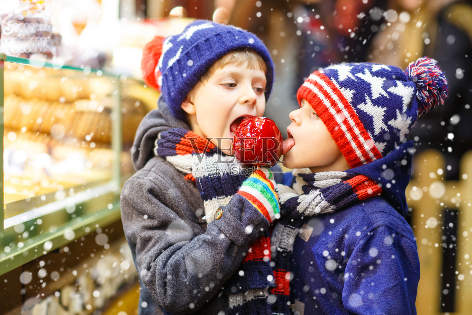 两个小男孩站在圣诞市场上吃着苹果糖照片摄影图片