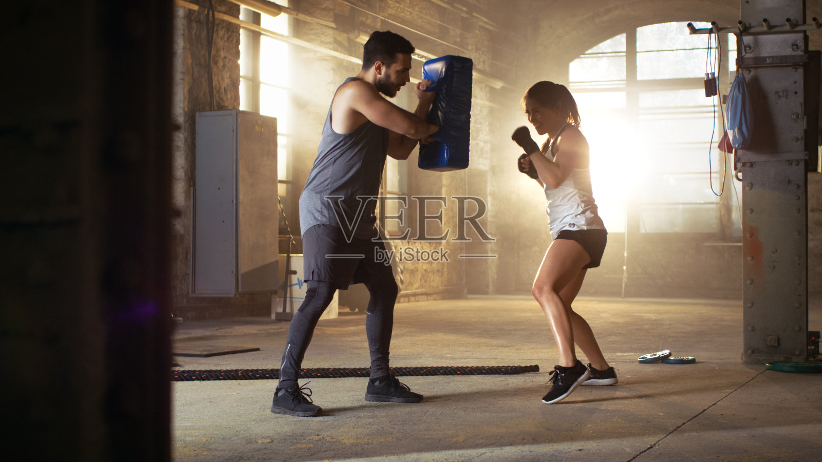 运动女子打拳击袋，她的伙伴/教练持有。她是职业拳击手，正在健身房里训练。照片摄影图片