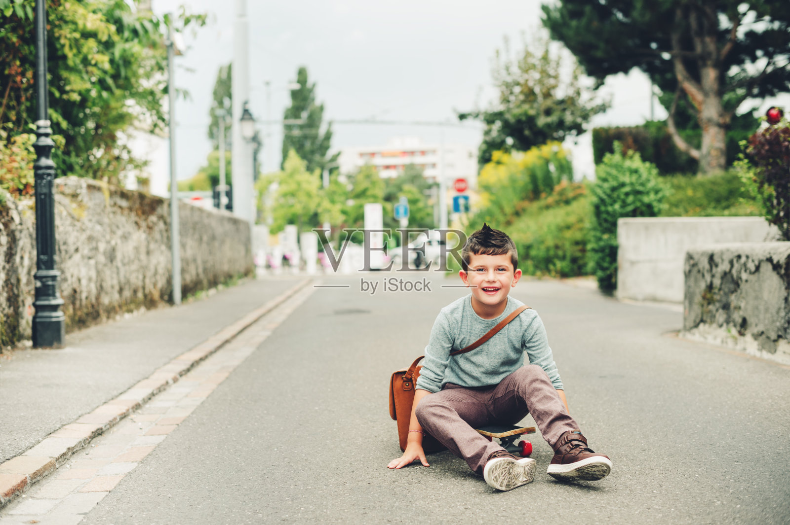 户外肖像滑稽的小男生穿着棕色皮包肩，骑滑板。回到学校的概念。电影看色调的形象照片摄影图片