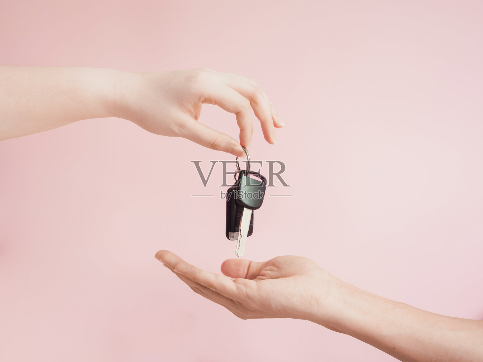 一名亚洲女性用美丽的手指和手把她的车钥匙给了新车主，并配上了粉色柔和的背景照片摄影图片