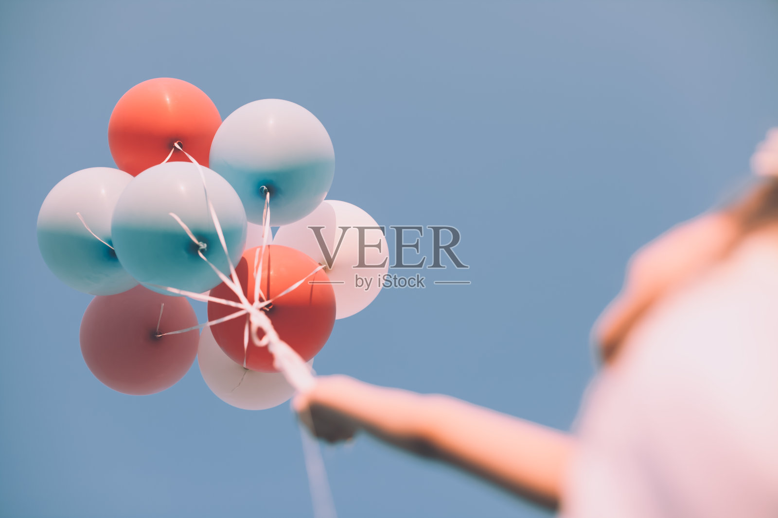 手握彩色气球的女孩在清澈的蓝色天空-低角度的观点照片摄影图片