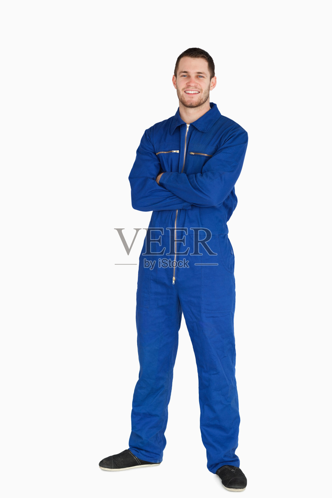 微笑的年轻机械师穿着连衫裤，双臂交叉照片摄影图片
