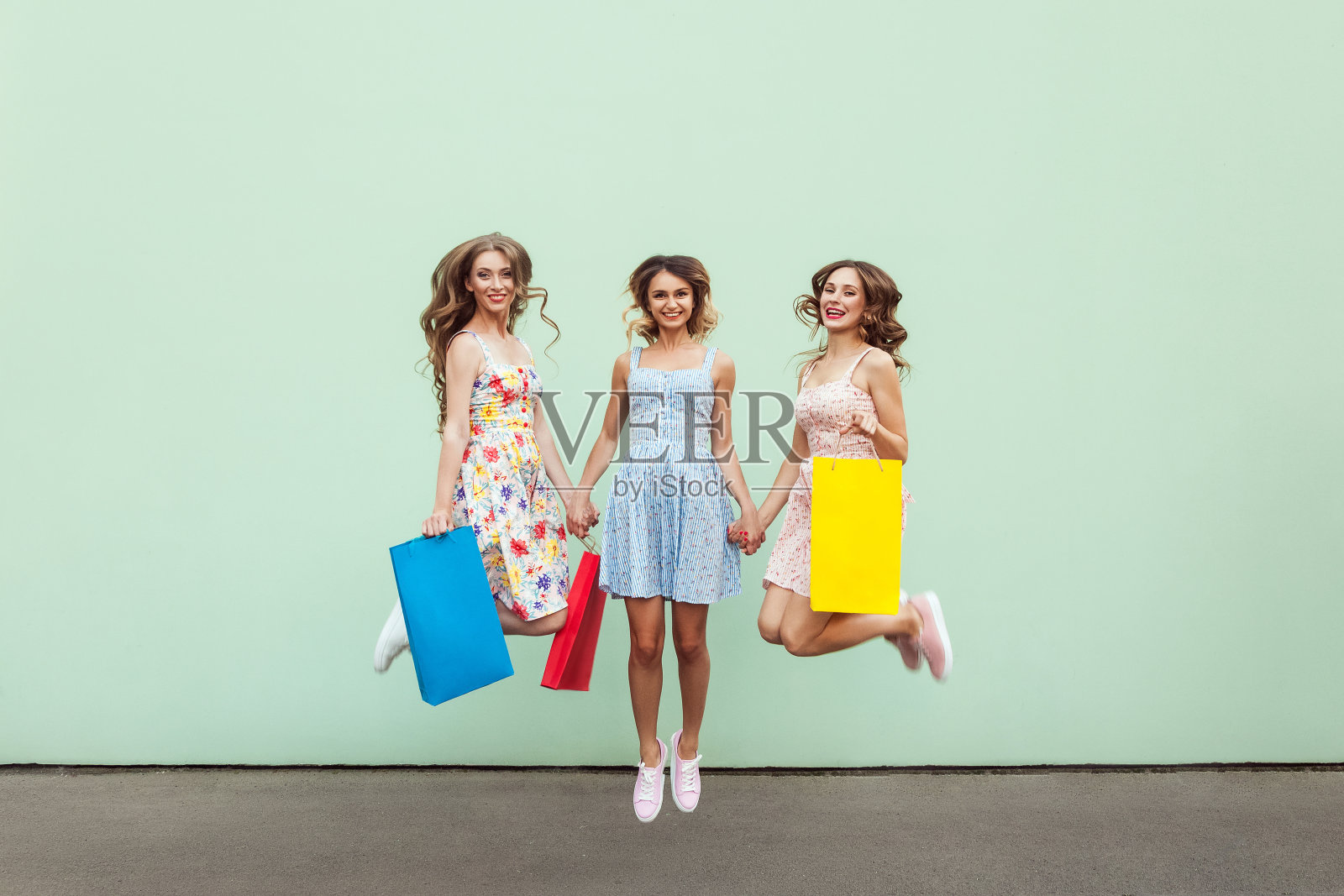 幸福美丽的三个朋友从快乐中跳出，带着五颜六色的包购物后。照片摄影图片