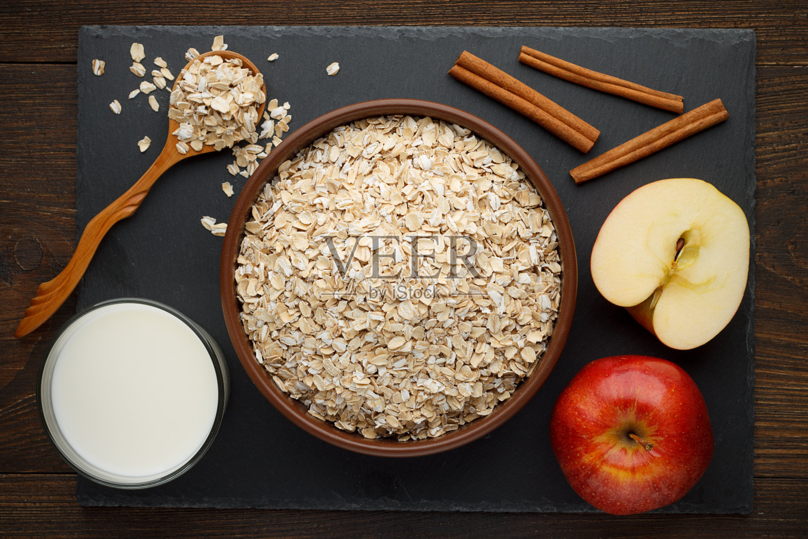 燕麦片卷在碗与苹果，肉桂和牛奶石板背景。照片摄影图片