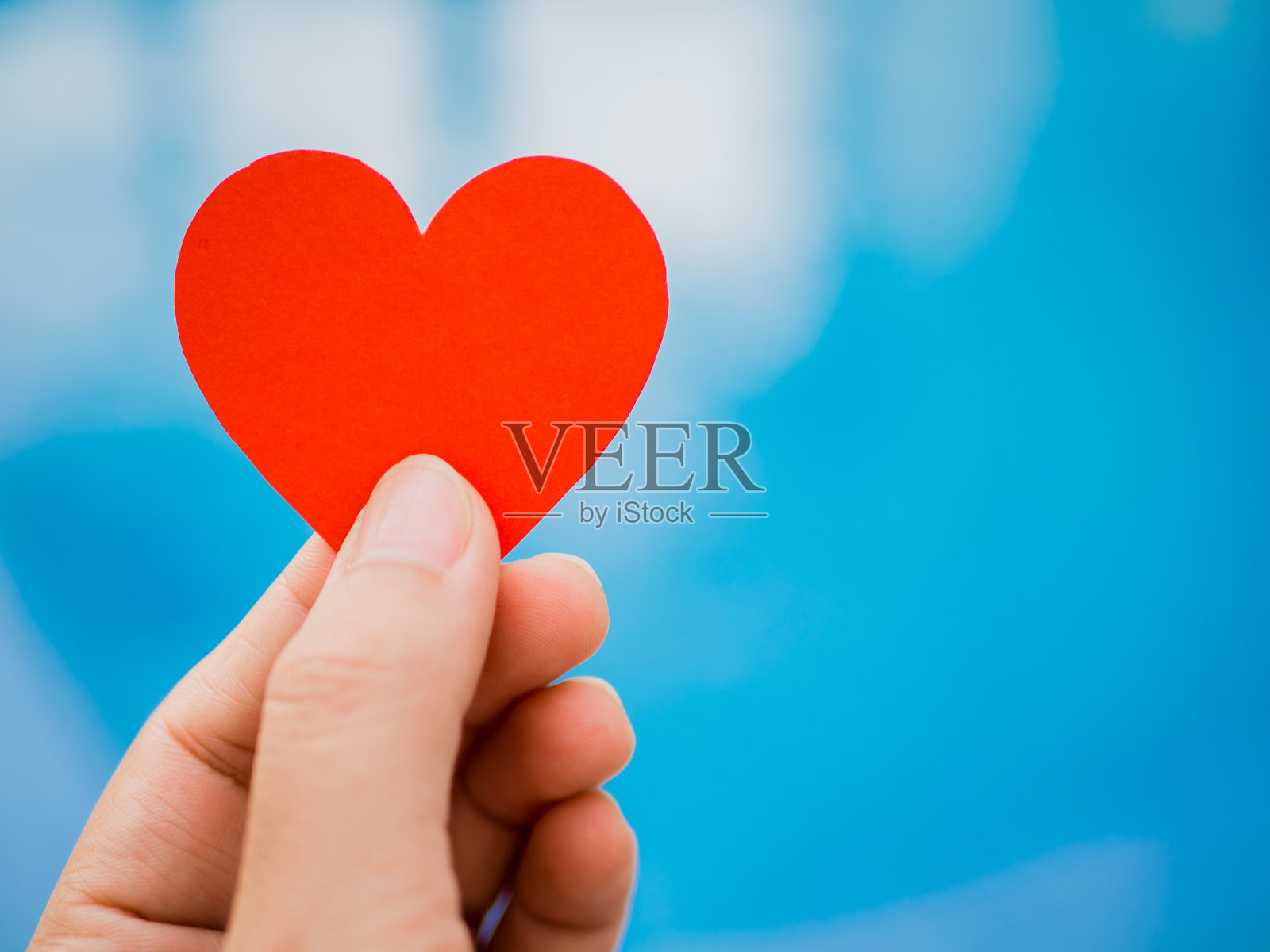 特写手握红纸心形在蓝色的背景。爱情和情人节的概念。照片摄影图片