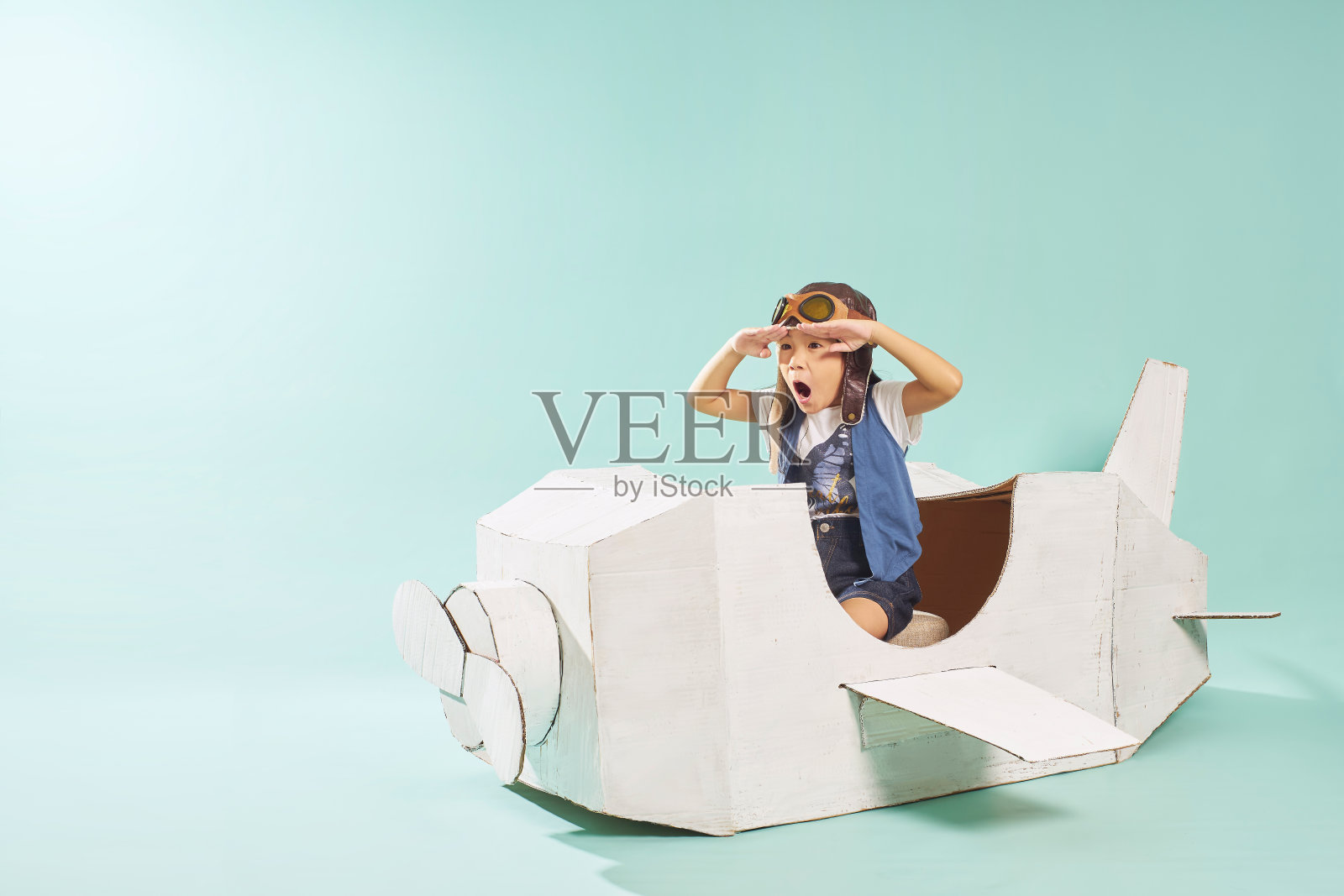 可爱的小女孩在玩纸板飞机。白色复古风格的纸板飞机在薄荷绿色的背景。童年的梦想想象概念。照片摄影图片