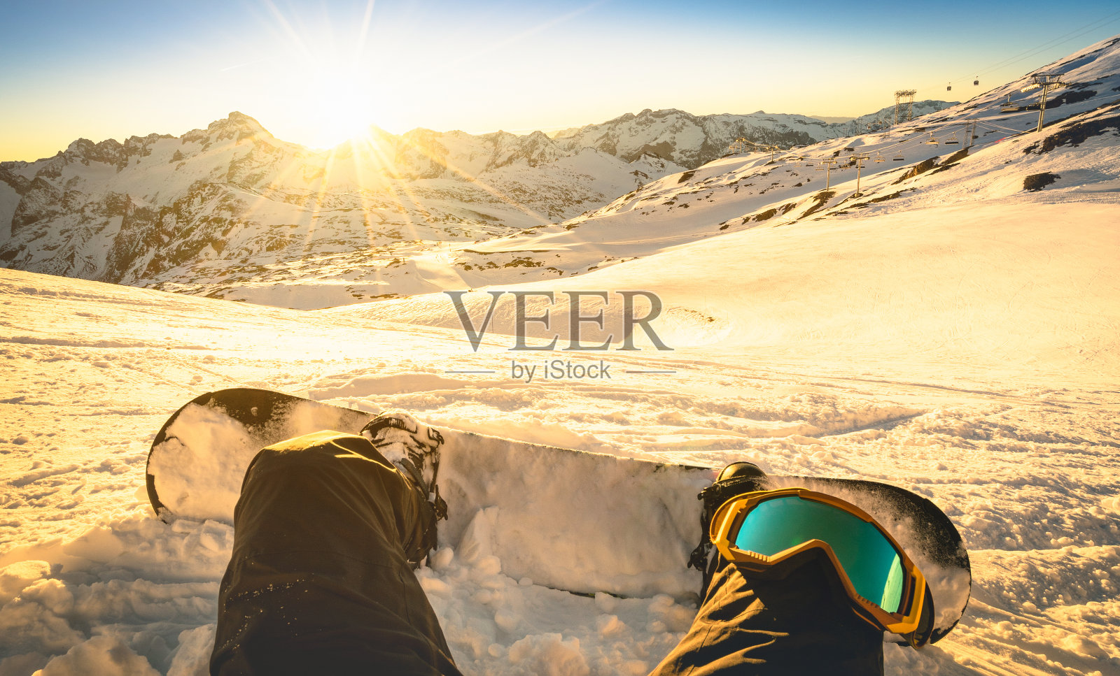 滑雪板坐在放松的时刻在公共滑雪胜地日落-冬季运动概念与人在山顶准备骑下来-腿的观点与温暖的背光滤镜照片摄影图片