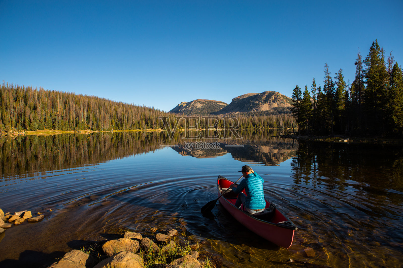 一名男子用桨将一只红色的独木舟划进湖中照片摄影图片
