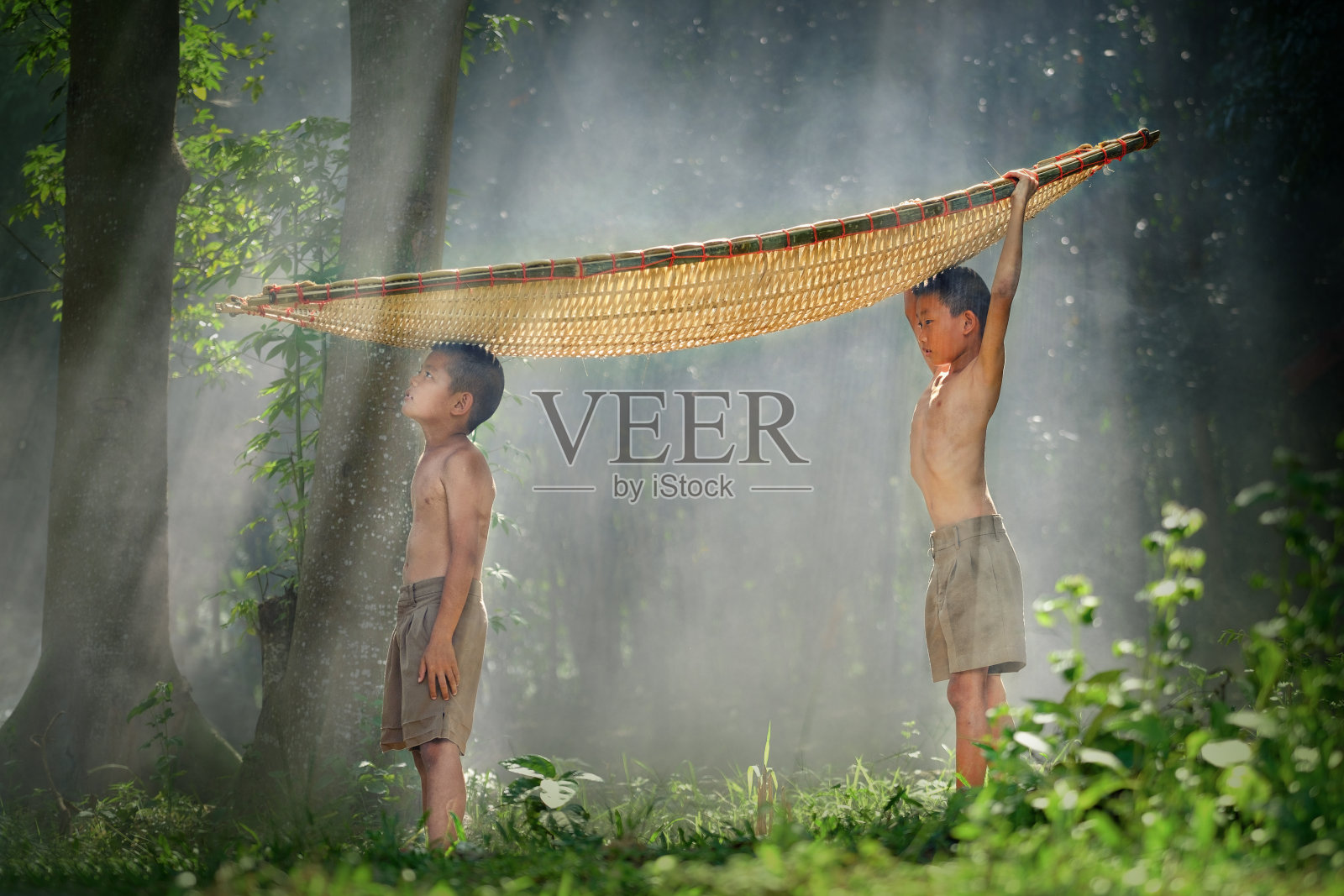 在泰国农村，两兄弟头顶竹船站在旁边。照片摄影图片