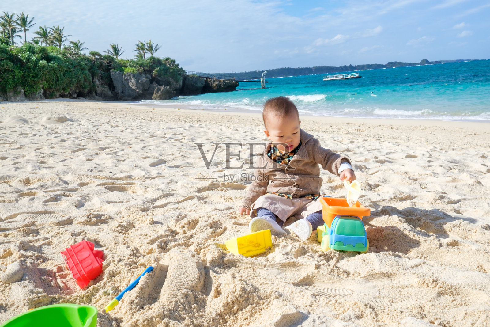 可爱的1 - 2岁亚洲小男孩坐在美丽的热带沙滩上玩玩具照片摄影图片
