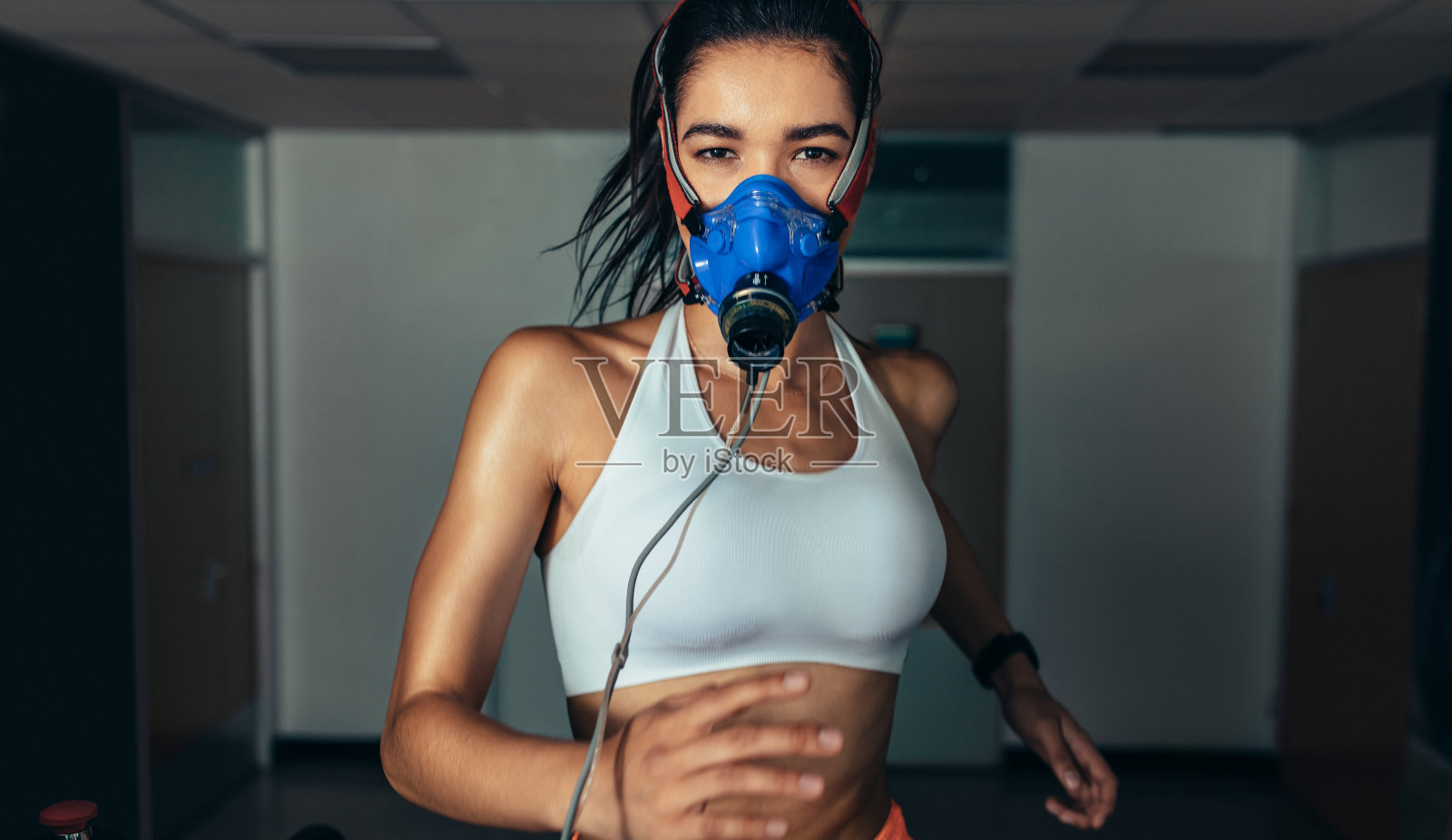 戴着面具在健身房跑步机上跑步的女运动员照片摄影图片