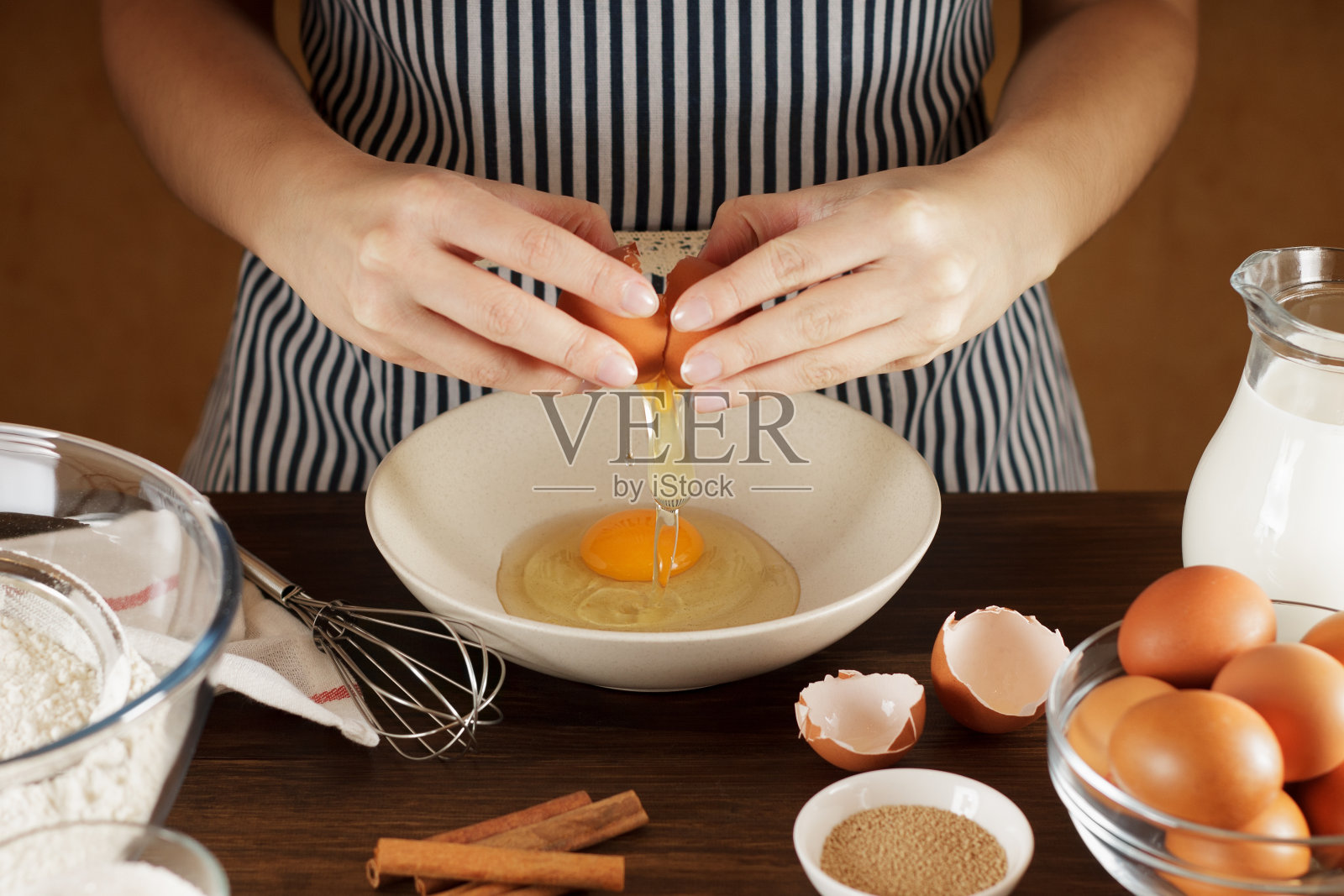 女性双手将鸡蛋打碎在厨房桌子上的陶瓷碗和餐具。照片摄影图片