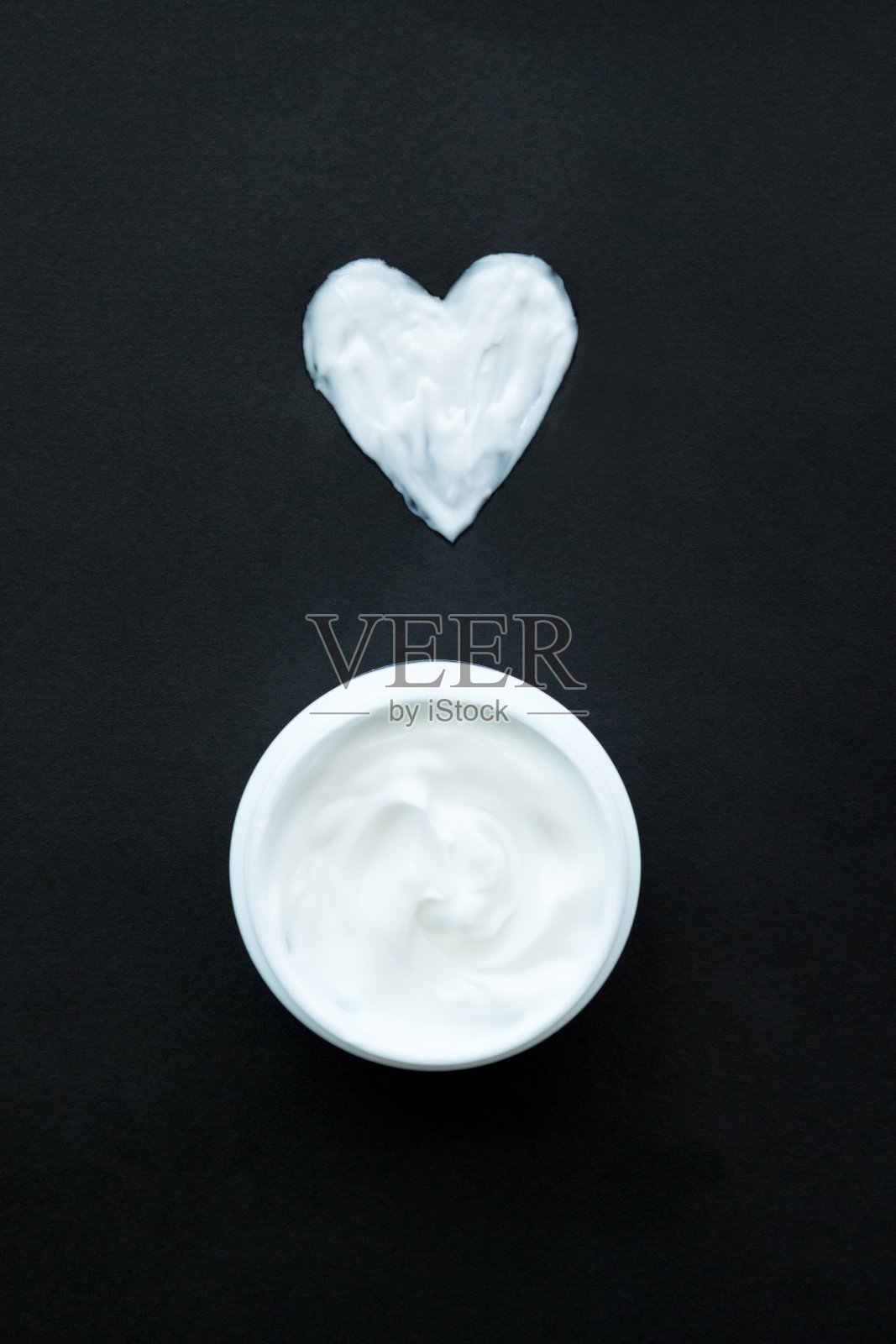 心形的奶油在黑色的背景。白色塑料容器内的面部或身体用霜。照片摄影图片
