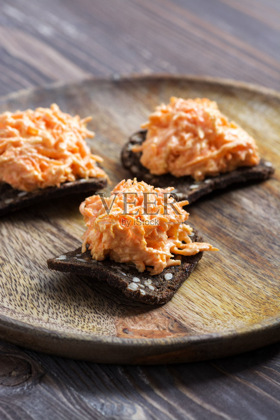 磨碎的胡萝卜和大蒜放在黑麦饼干上，装在木盘子里。照片摄影图片