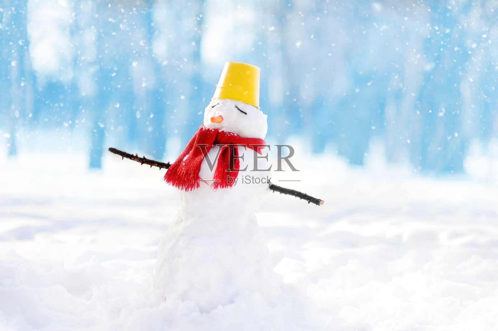 在蓝色背景的雪景公园里，用围巾、桶帽和鼻子胡萝卜手工制作的雪人照片摄影图片