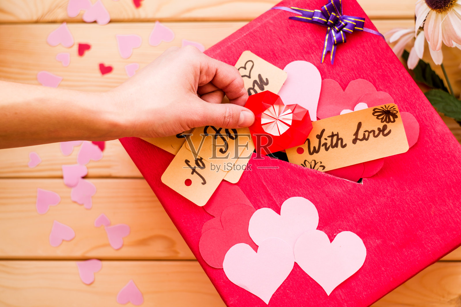 女人的手把一个折纸心放在情人节的红色礼盒上，盒子上有一个空隙用来放情人节的纸照片摄影图片