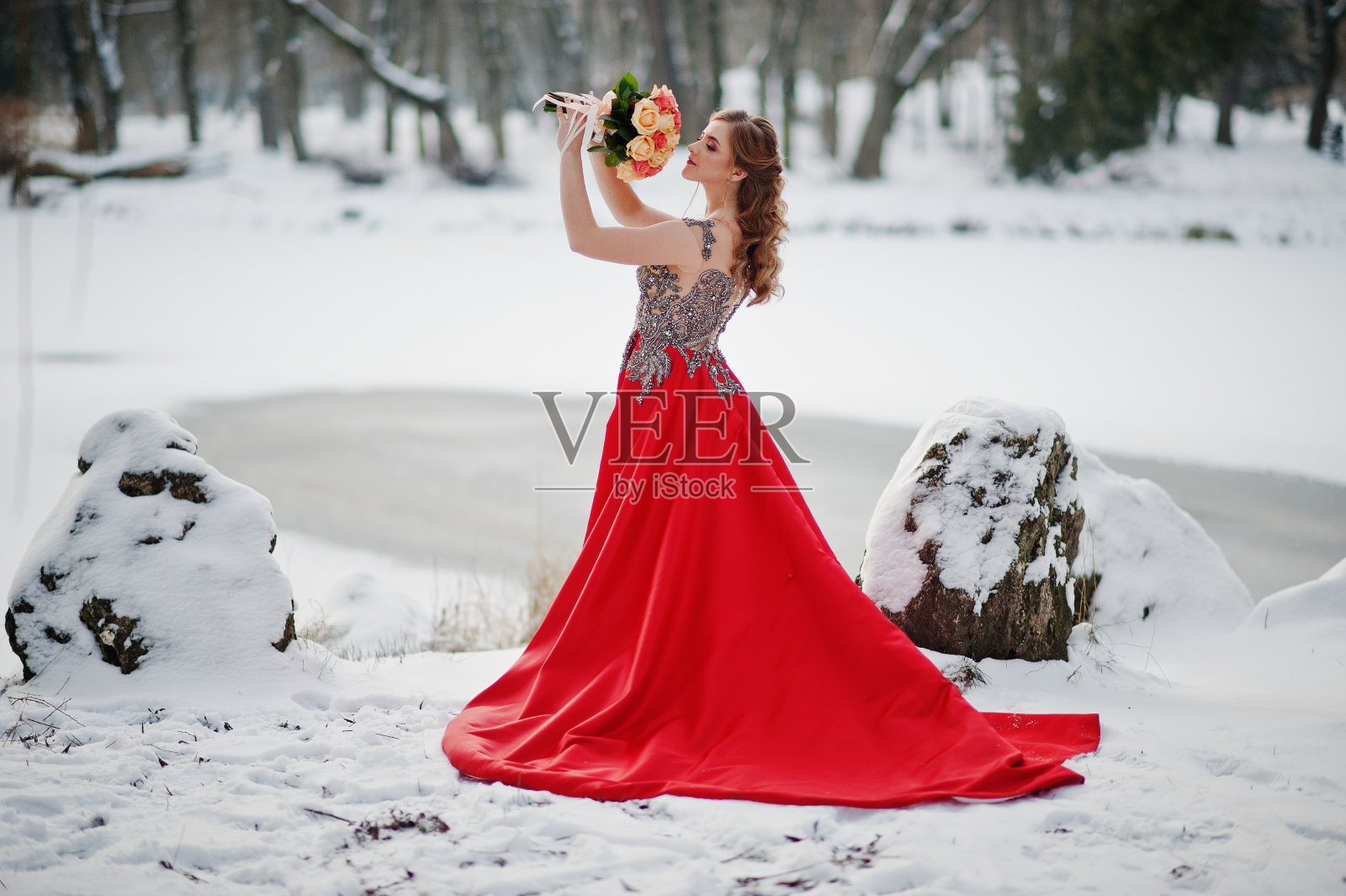 美丽的女孩在冬天穿着优雅的红裙子拿着花束。照片摄影图片