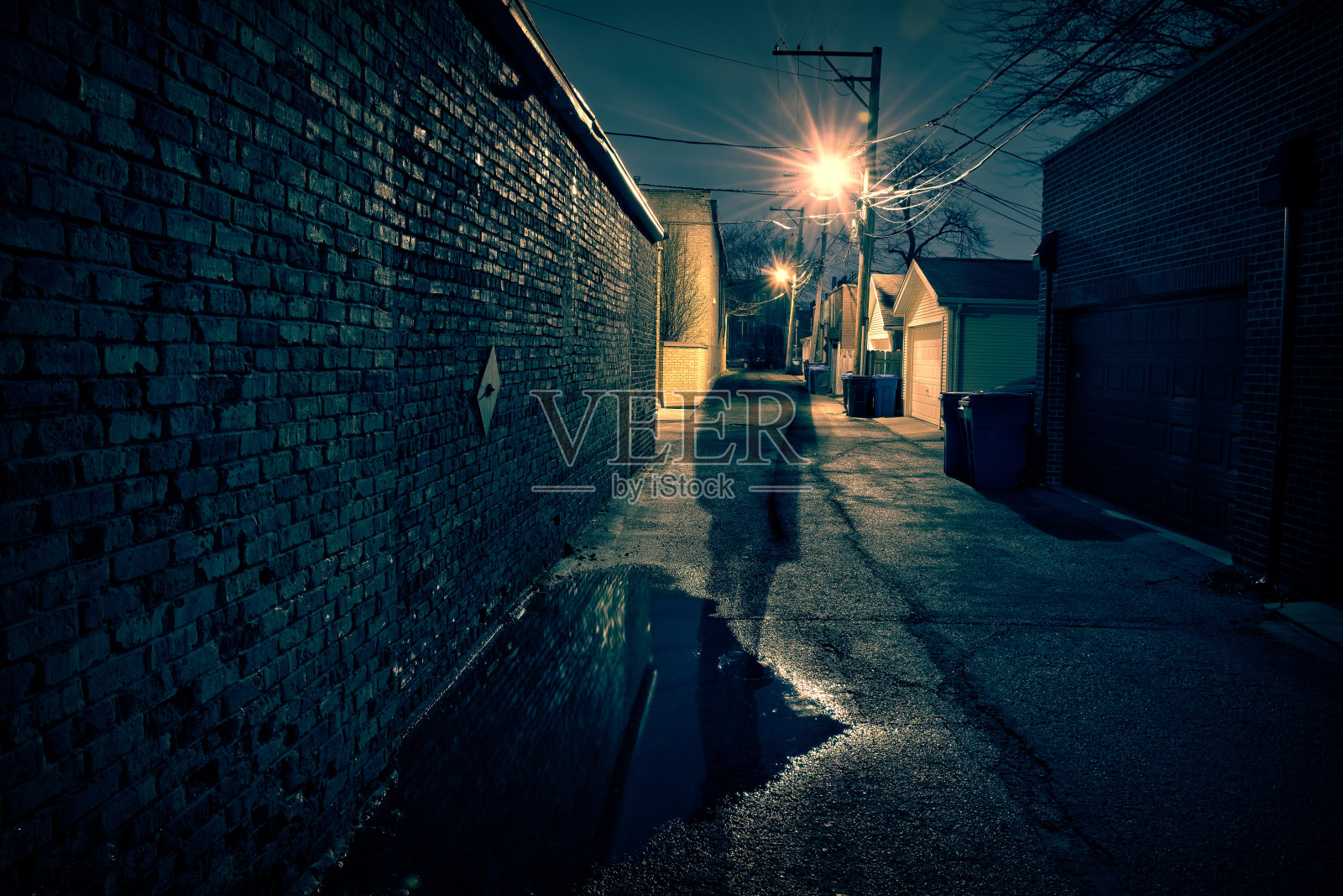 一个可怕的人的影子在一个黑暗和可怕的城市小巷雨后的夜晚。照片摄影图片